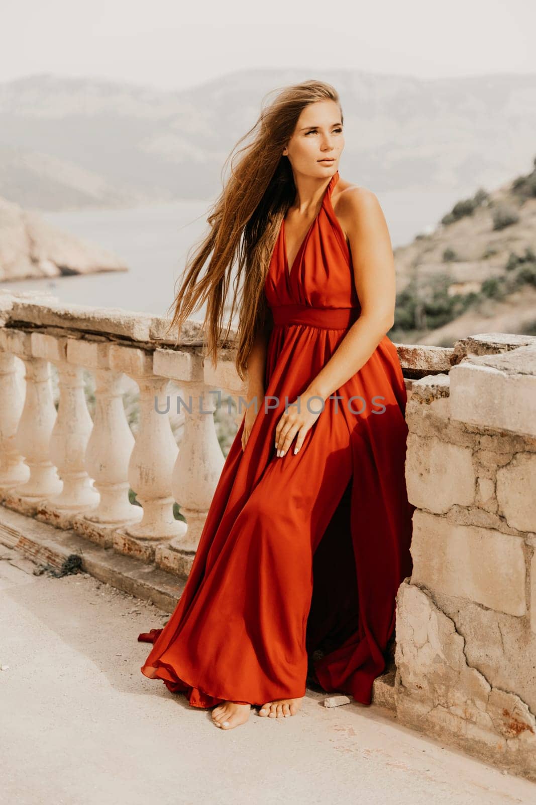 Woman red dress. Summer lifestyle of a happy woman posing near a fence with balusters over the sea