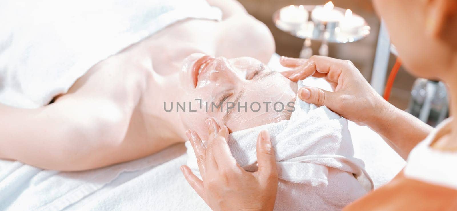 Portrait of beautiful caucasian woman having facial massage with homemade facial mask while lies on spa bed surrounded by beauty electrical equipment and peaceful nature environment. Tranquility.