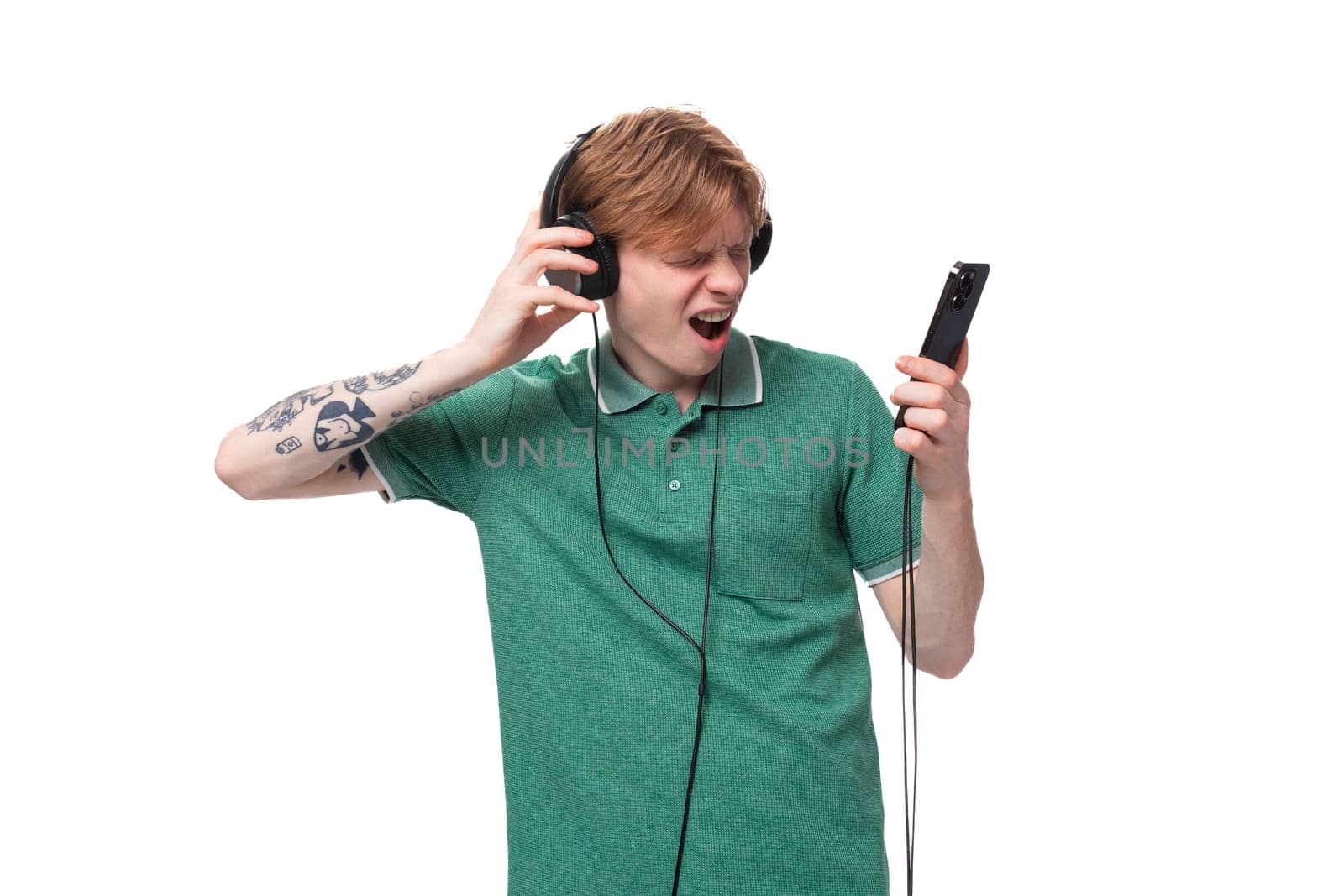 a young energetic bright red-haired caucasian guy in a green t-shirt dances to the music from the headphones from his favorite playlist.