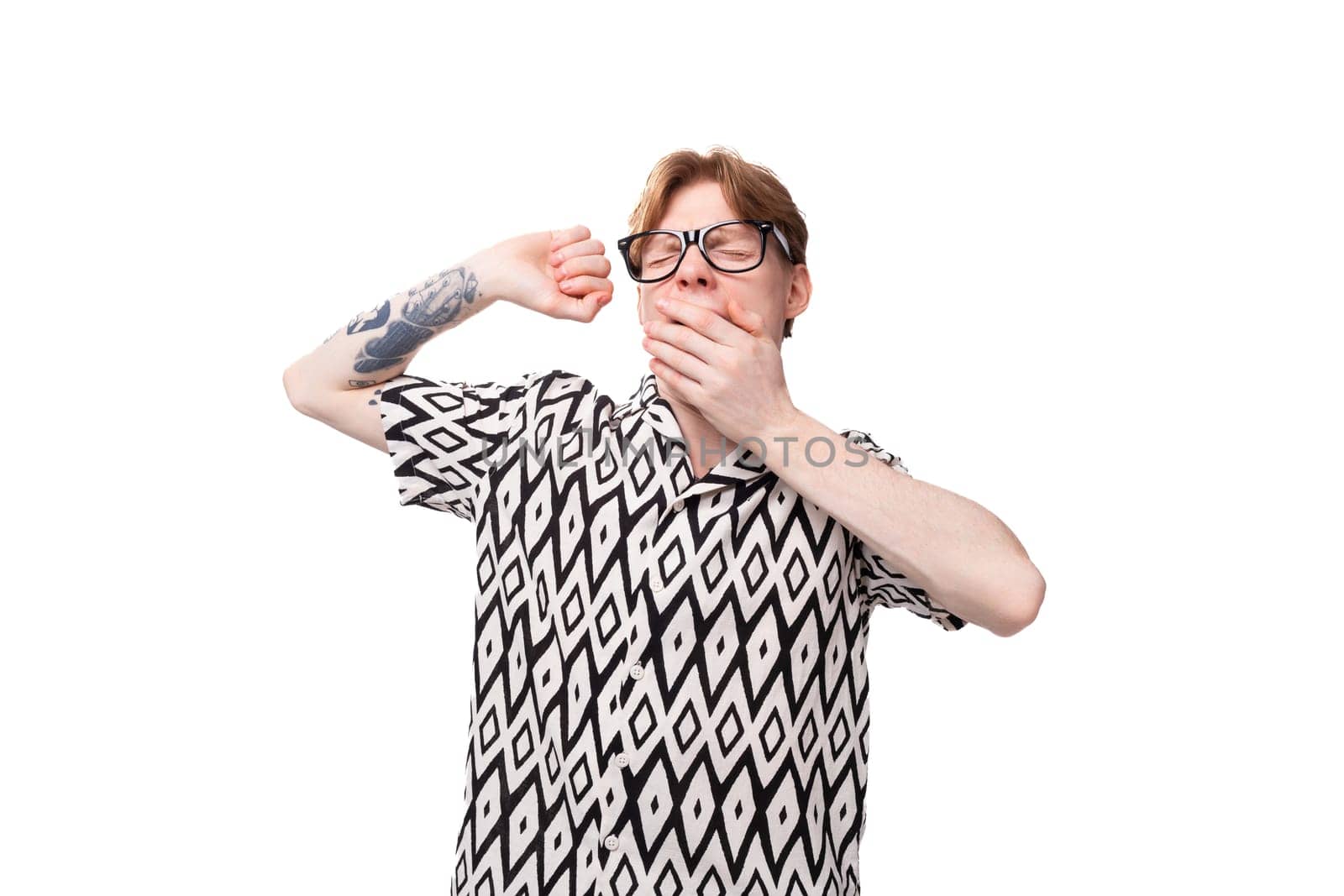 young handsome caucasian man with reddish golden hair in black and white summer shirt yawns.