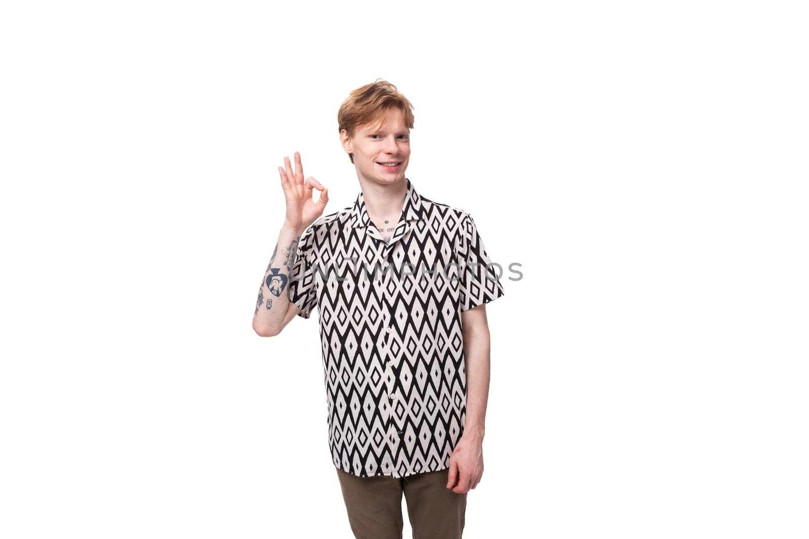 young caucasian man with red hair with a tattoo is dressed in a summer black and white shirt on a background with copy space.