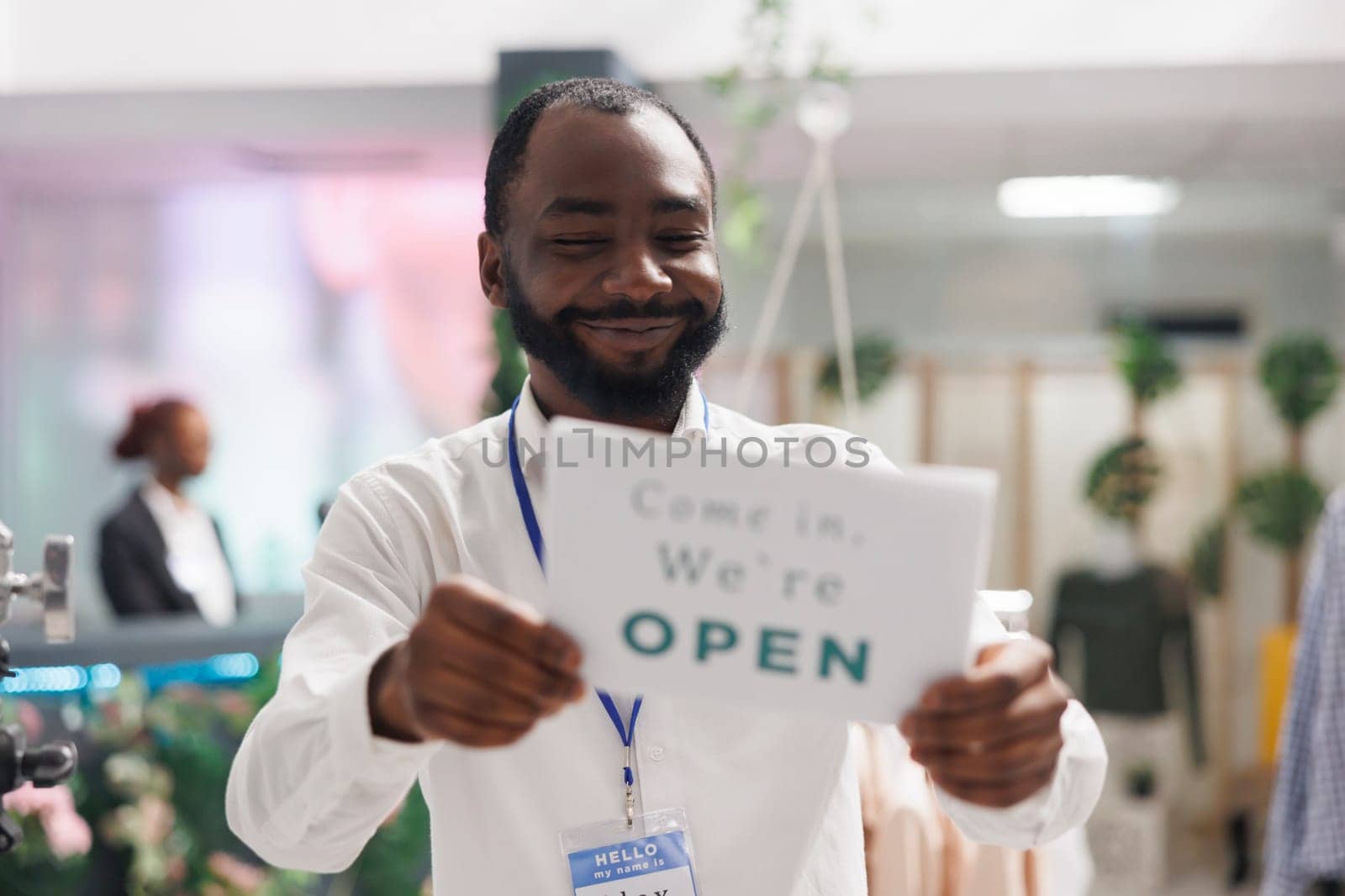 Clothes store smiling cheerful assistant hanging opening sign on front door. Happy african american fashion boutique manager holding sign board with come in text message