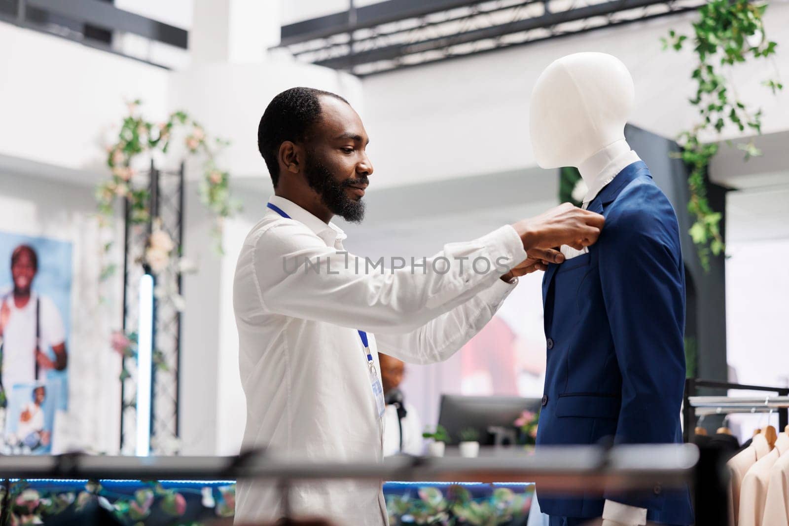 Clothes retail shop assistant dressing mannequing in formal suit by DCStudio