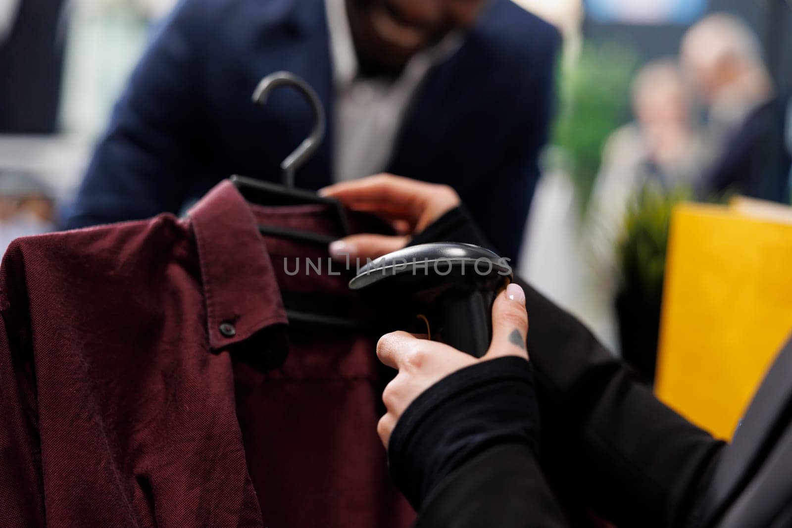 Showroom worker scanning elegant shirt using store scanner, preparing purchase for african american shopper. Fashionable customer buying trendy merchandise and clothes in shopping center. Close up