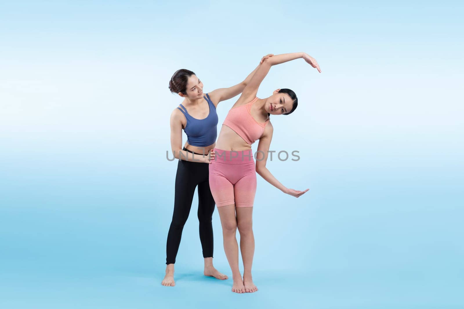 Asian woman in sportswear doing yoga exercise in standing pose with her trainer or yoga buddy. Healthy body care and meditation yoga lifestyle in full shot on isolated background. Vigorous