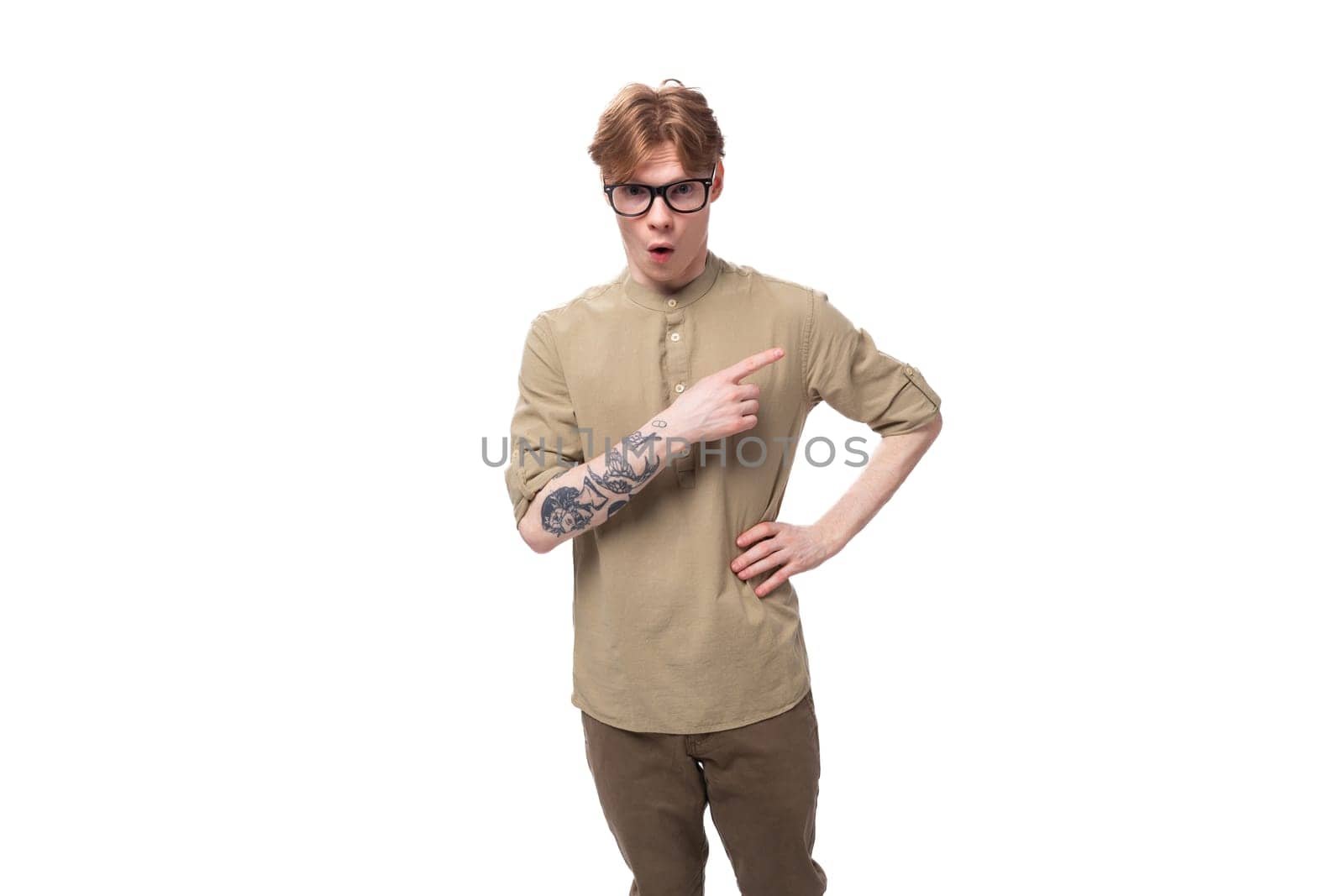 handsome young red-haired man in a beige shirt wears eyeglasses on a white background.