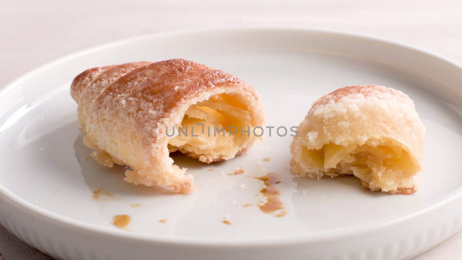 Small croissants in white ceramic plates, homemade cakes on concrete table top.