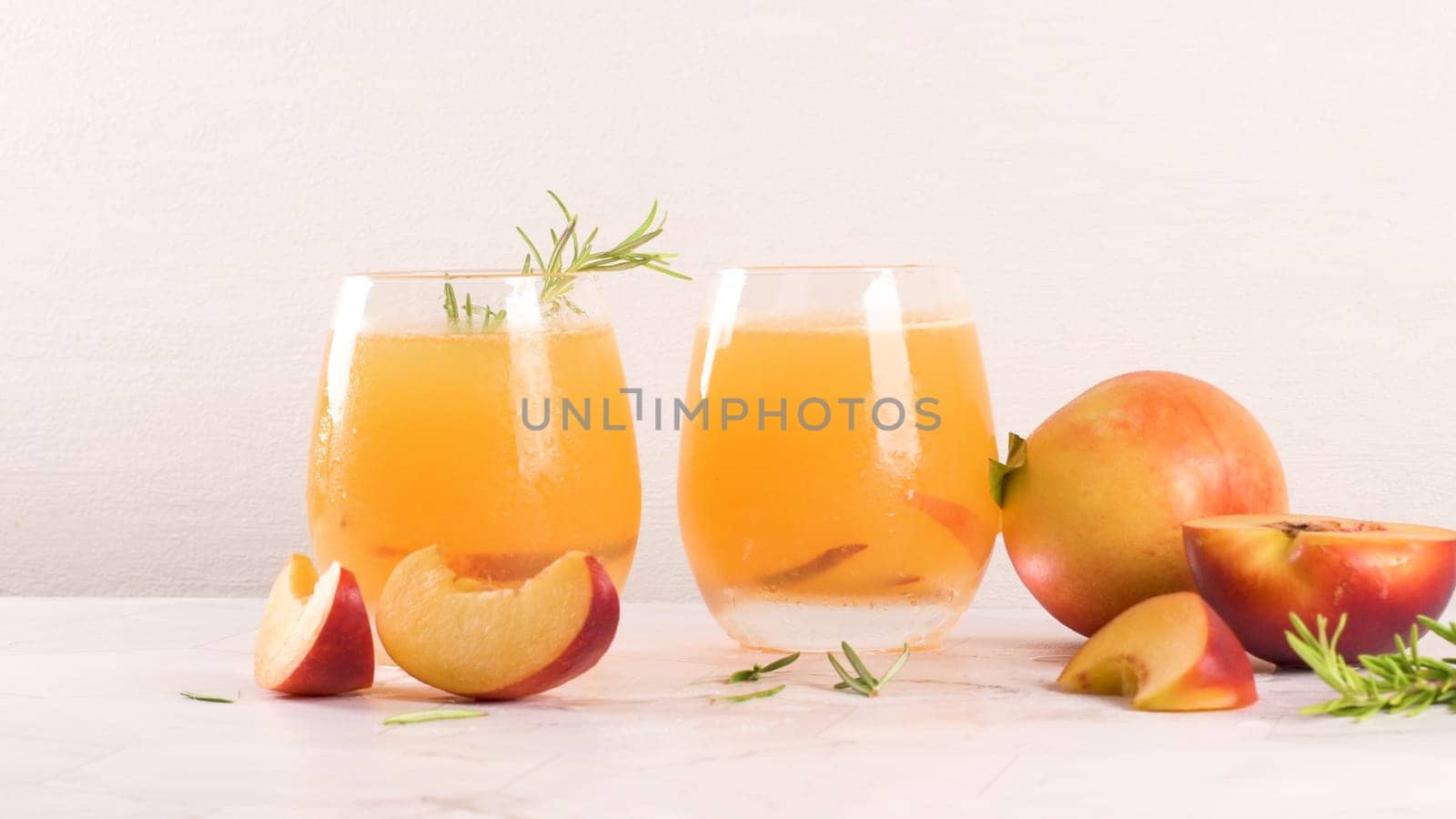 Homemade peach juice with ice cubes and rosemary leaves in glass on marble stone background.