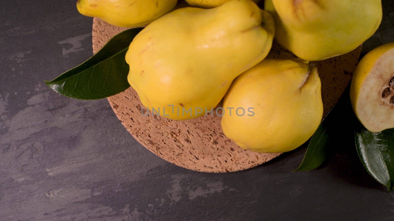 Ripe yellow quinces or queen apple fruits and sliced quince halves with seeds in craft cork plates on black rustic background.