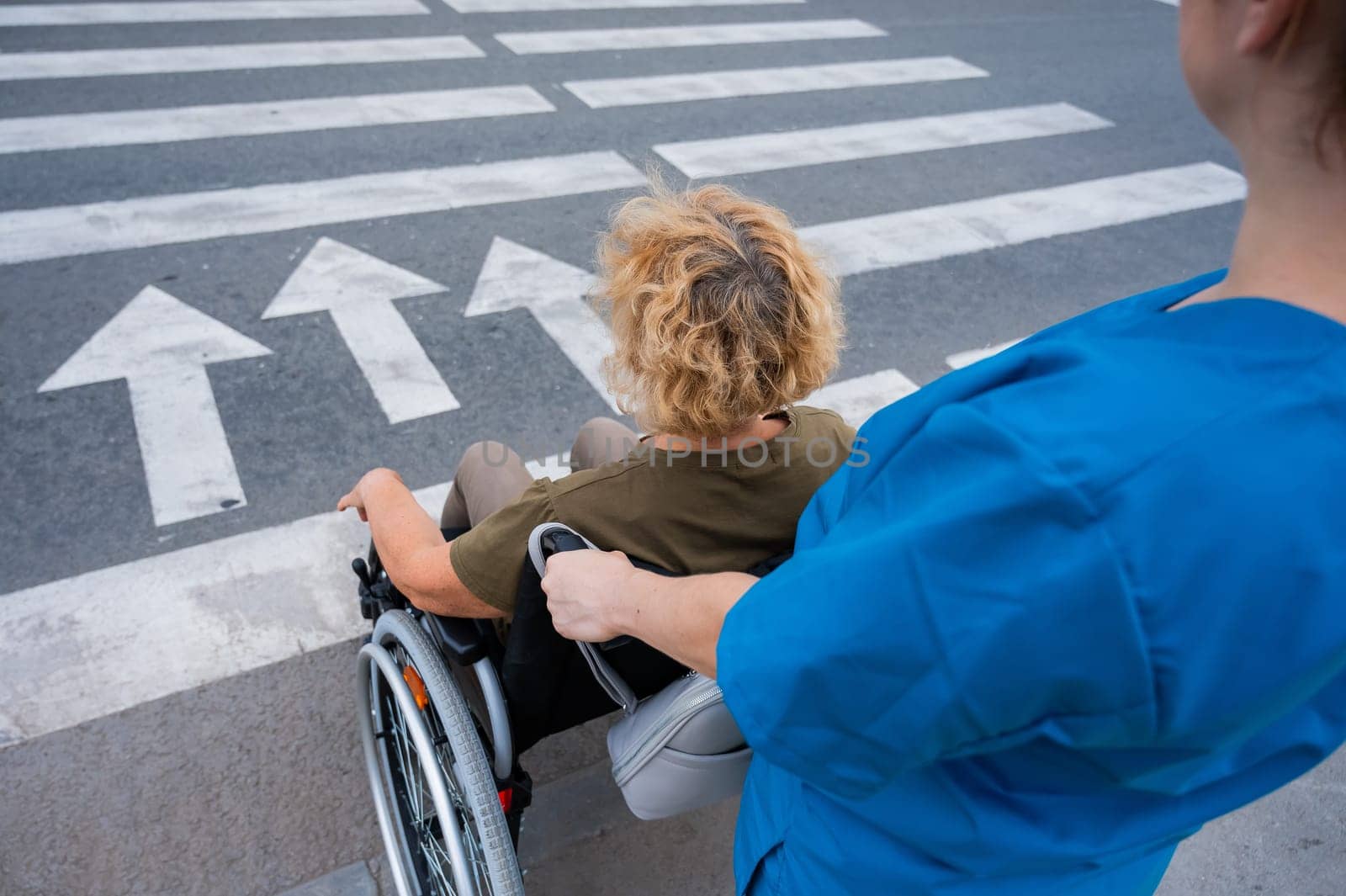 Rear view of a nurse helping an elderly woman in a wheelchair cross the road. by mrwed54