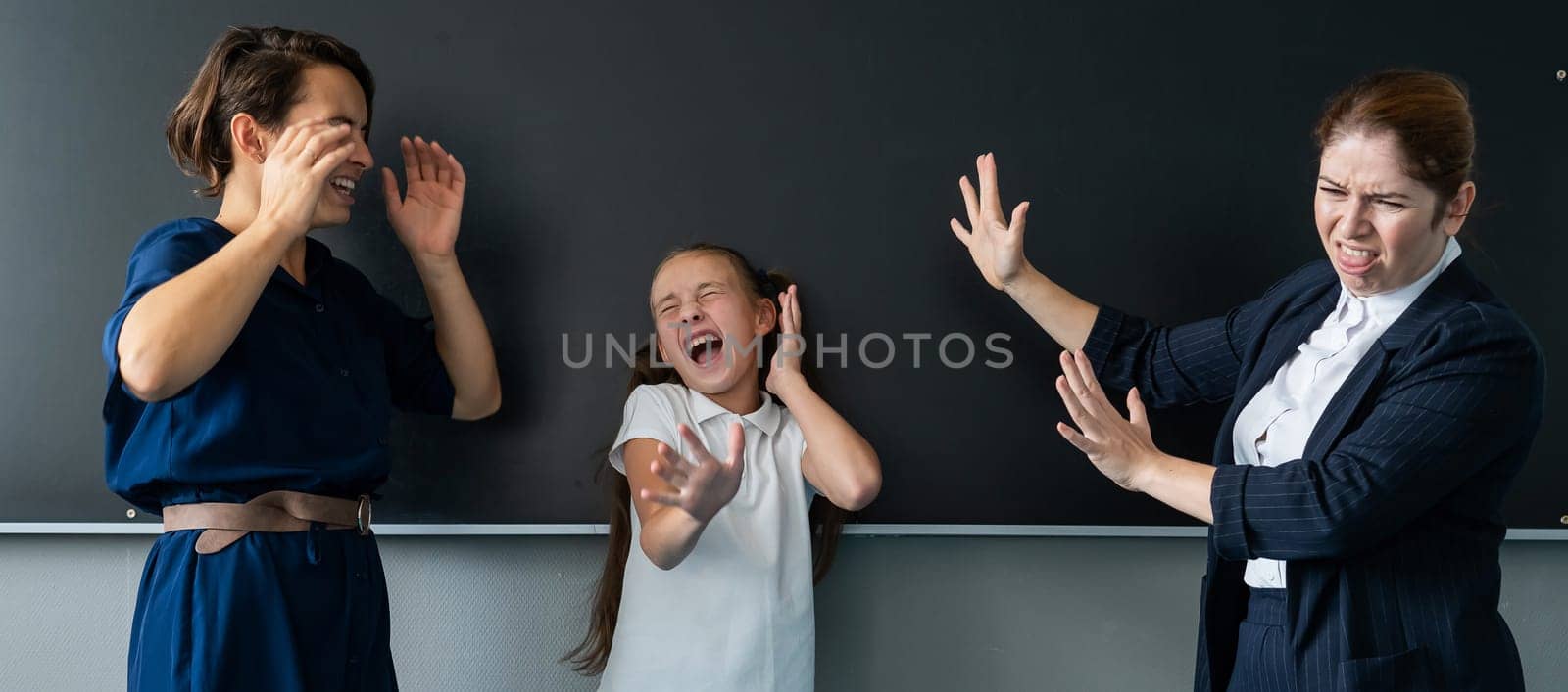 The female teacher screams at the schoolgirl and her mother standing at the blackboard