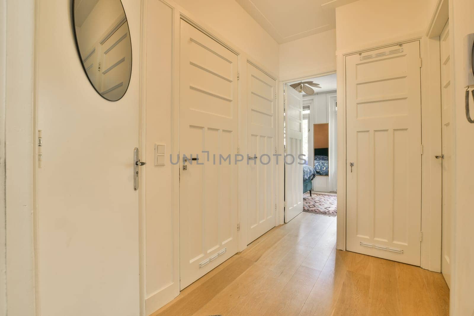 a long hallway with white doors and wood flooring on either side by side, looking into the living room