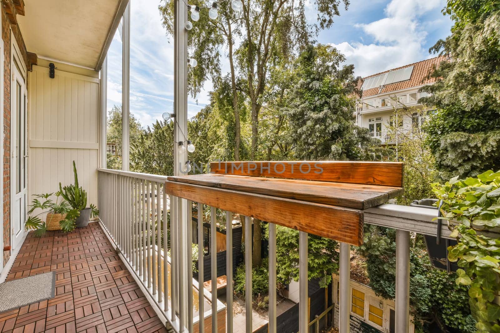 a balcony with brick flooring and white railings, surrounded by lush green trees on the other side of the house