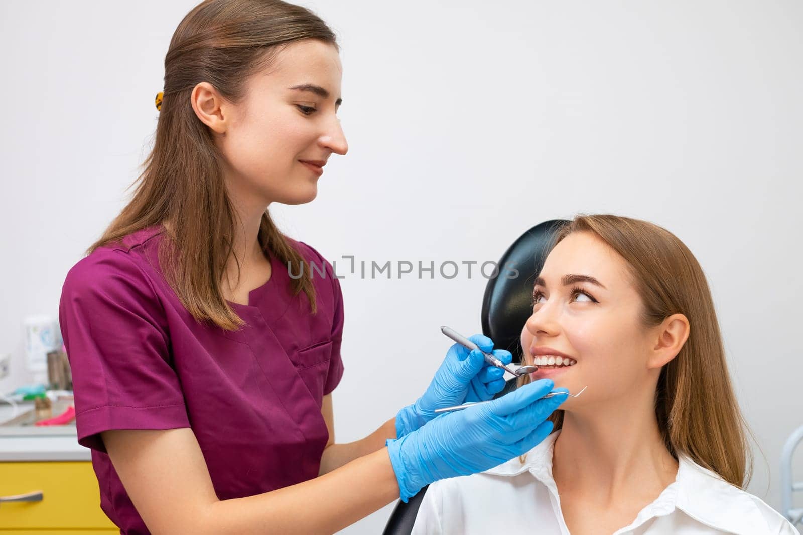 Cheerful female dentist holding dentist tool near smiling young patient by vladimka