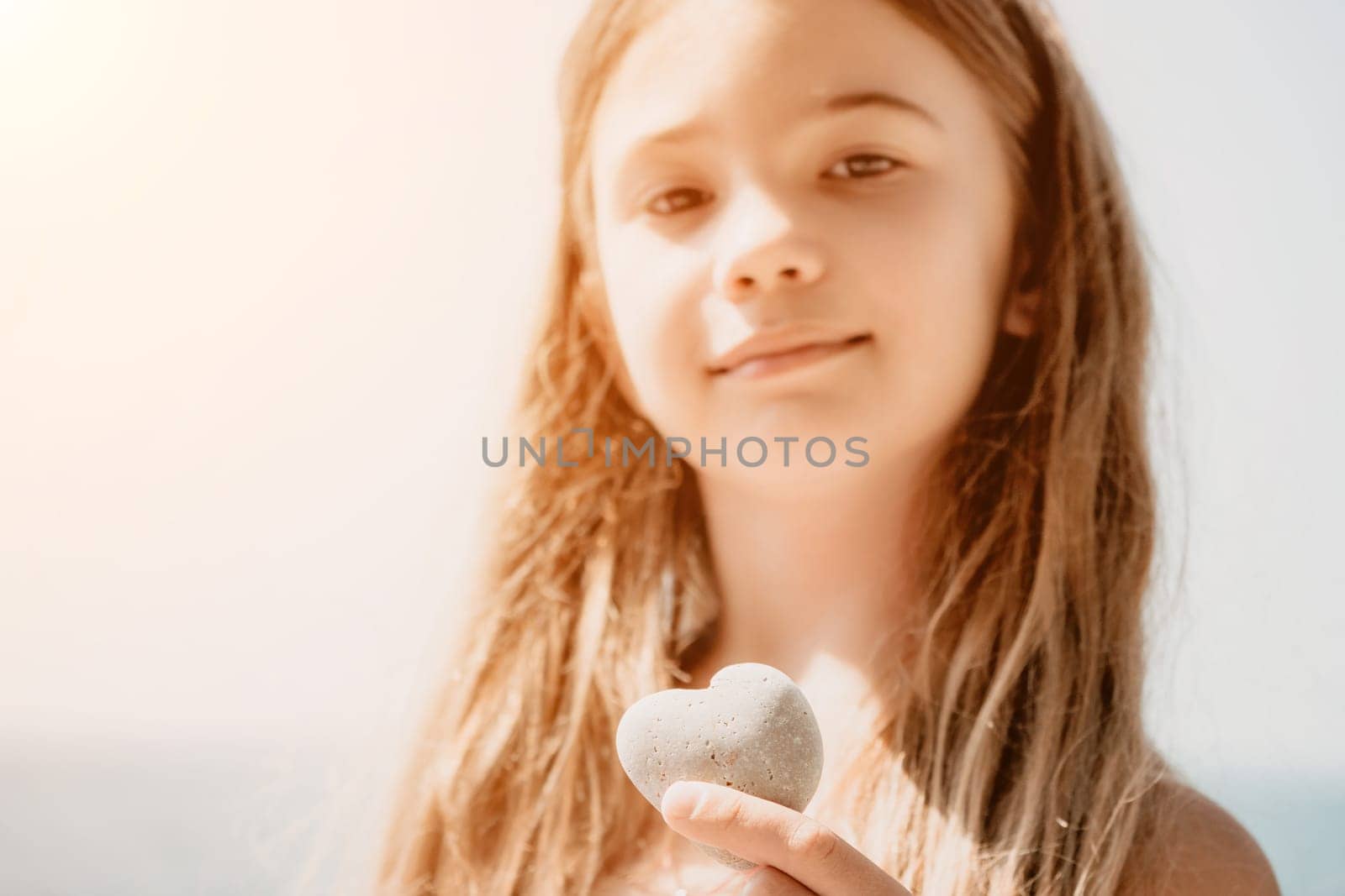 Female hand holding a stone in the shape of a heart against the background of the sea