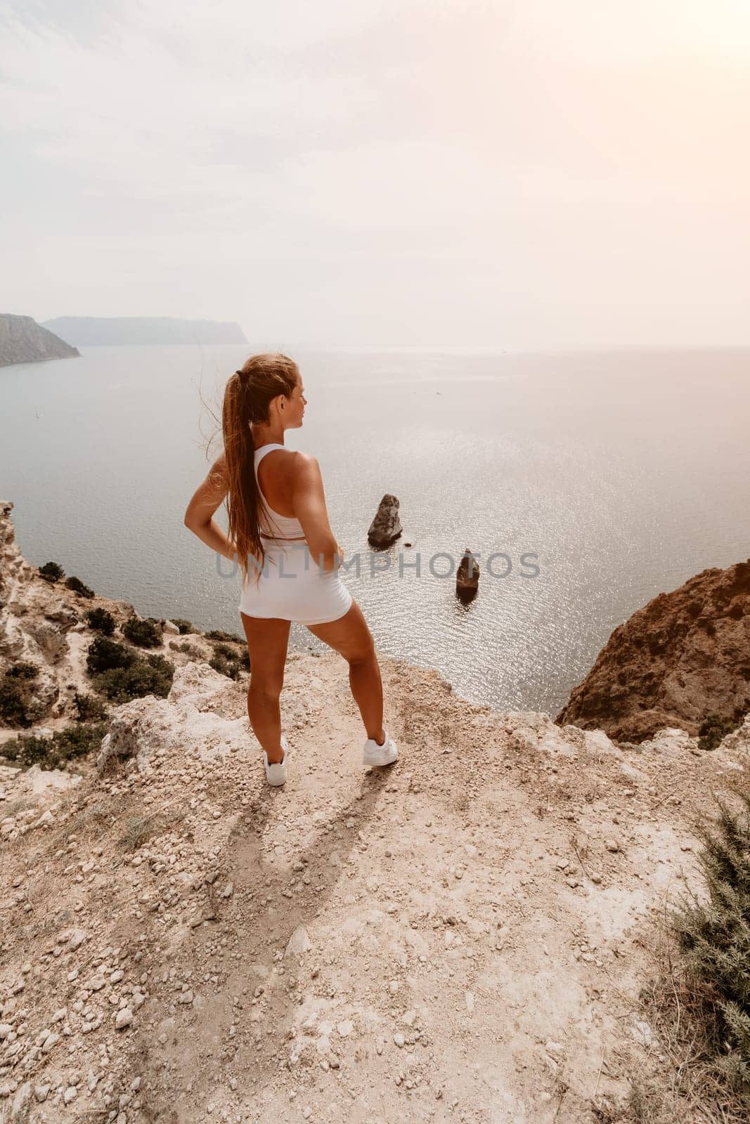 Woman travel sea. Happy tourist in hat enjoy taking picture outdoors for memories. Woman traveler posing on the beach at sea surrounded by volcanic mountains, sharing travel adventure journey