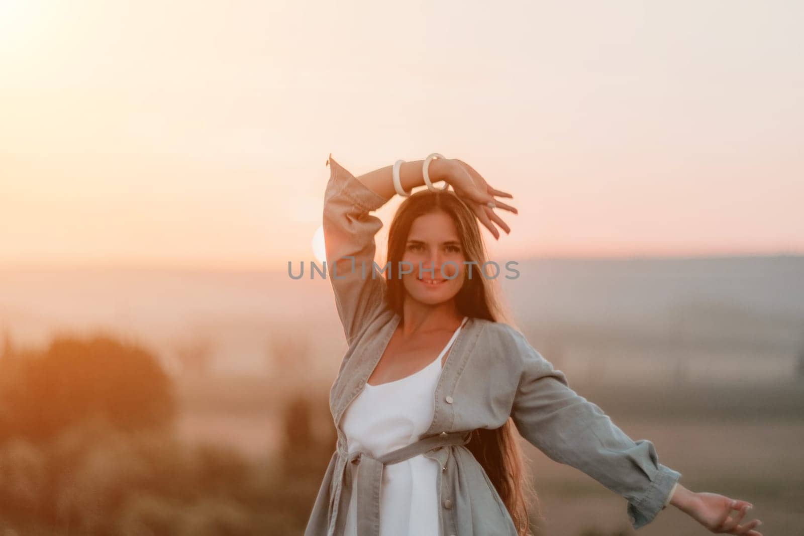 Romantic beautiful bride in white dress posing with sea and mountains in background. Stylish bride standing back on beautiful landscape of sea and mountains on sunset