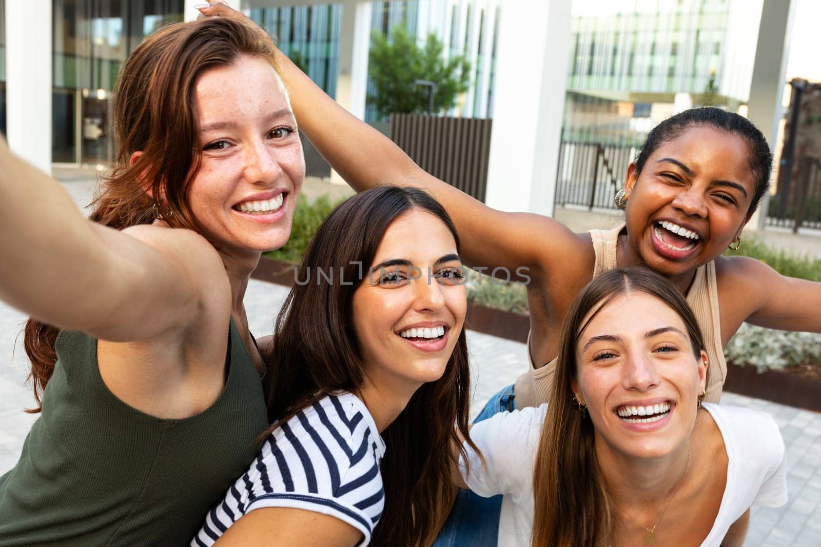 Selfie of happy girl friends looking at camera excited. smiling group of multiracial women having fun together outdoors. by Hoverstock