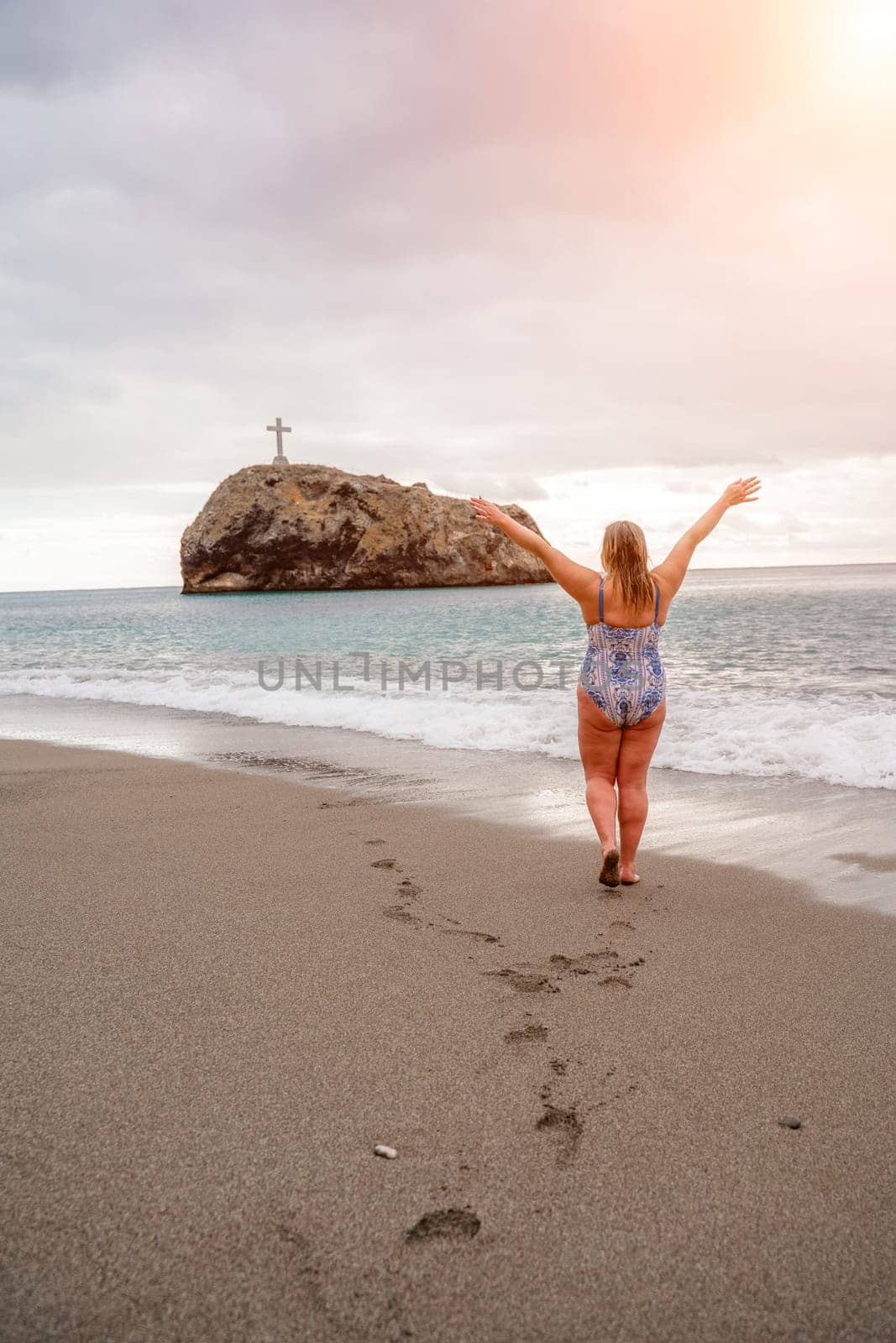 A plump woman in a bathing suit enters the water during the surf. Alone on the beach, Gray sky in the clouds, swimming in winter