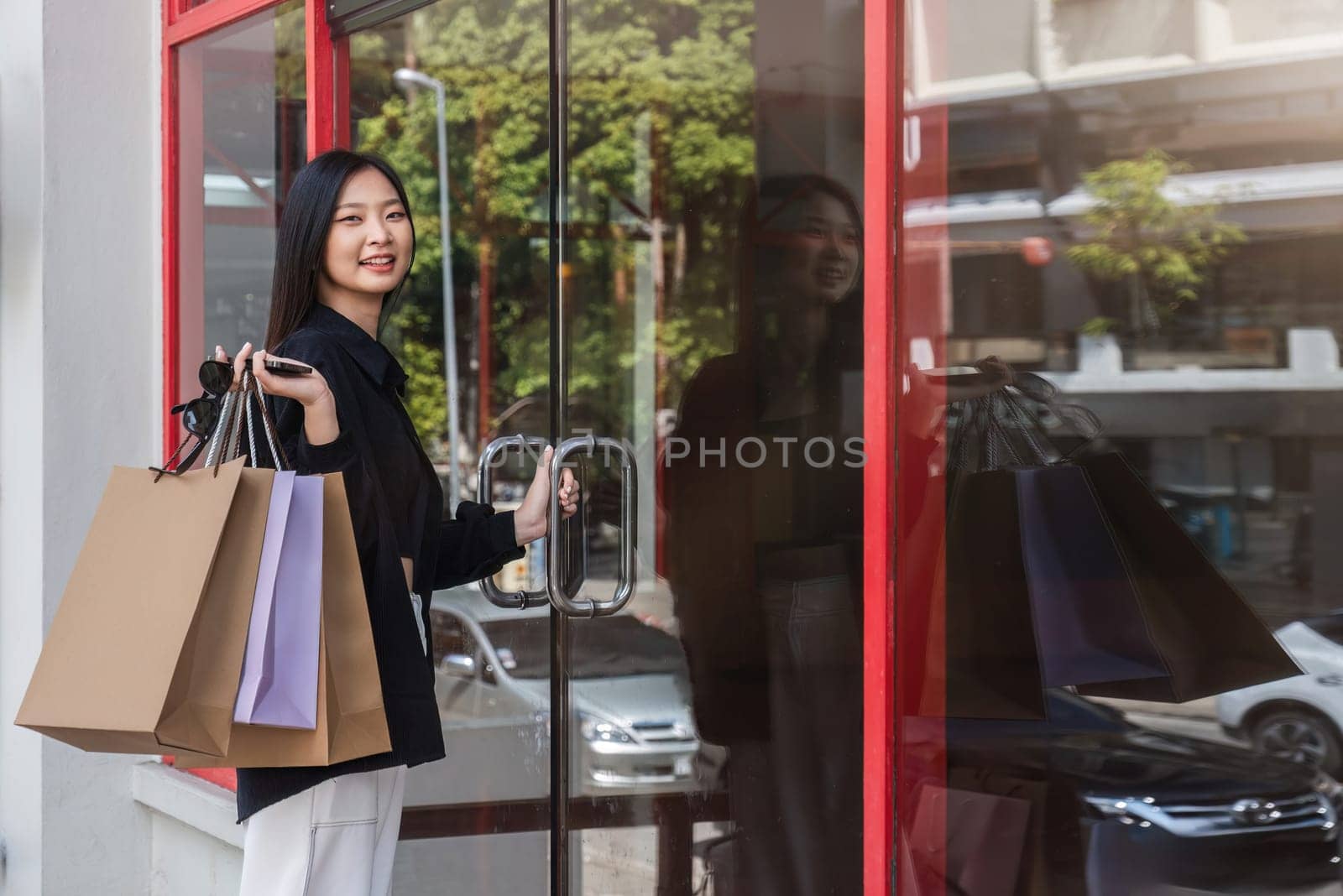 Asian woman using smartphone and looking away while enjoying a day shopping. Black Friday sale and discount. Buying clothes presents for holidays.