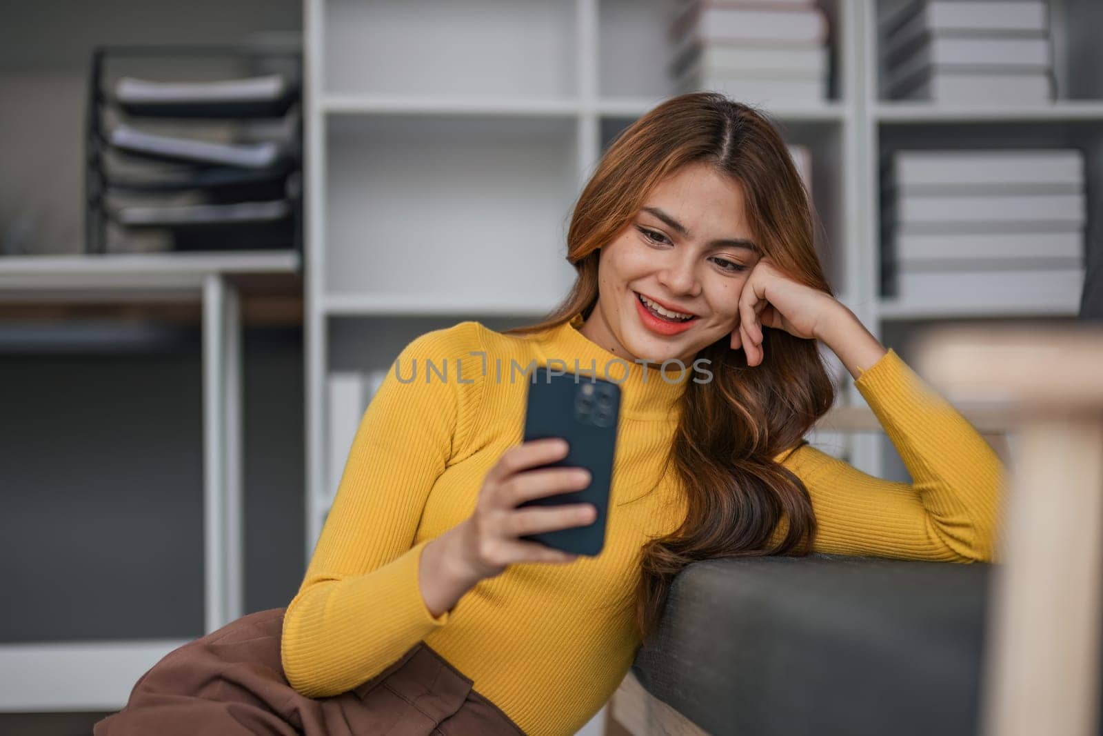Happy Asian woman playing with mobile phone while sitting on sofa at home Young woman smiling relaxedly with headphones in the morning It's time to rest..