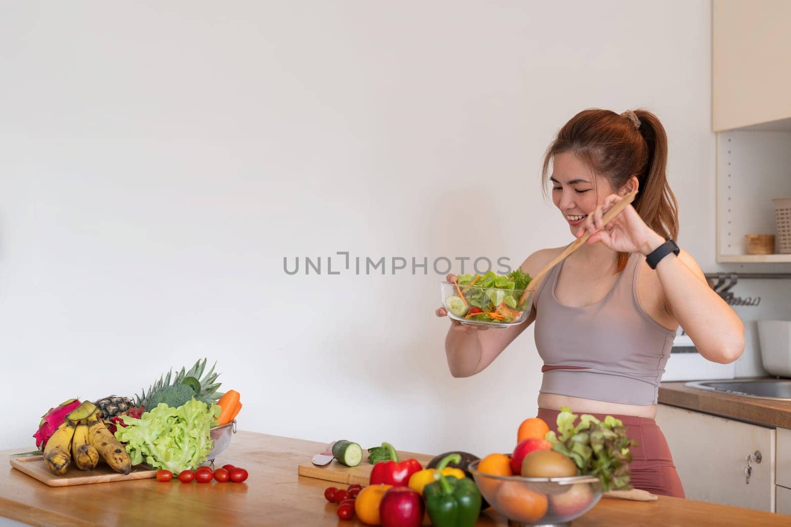 Young woman standing in the kitchen making a salad for health by nateemee