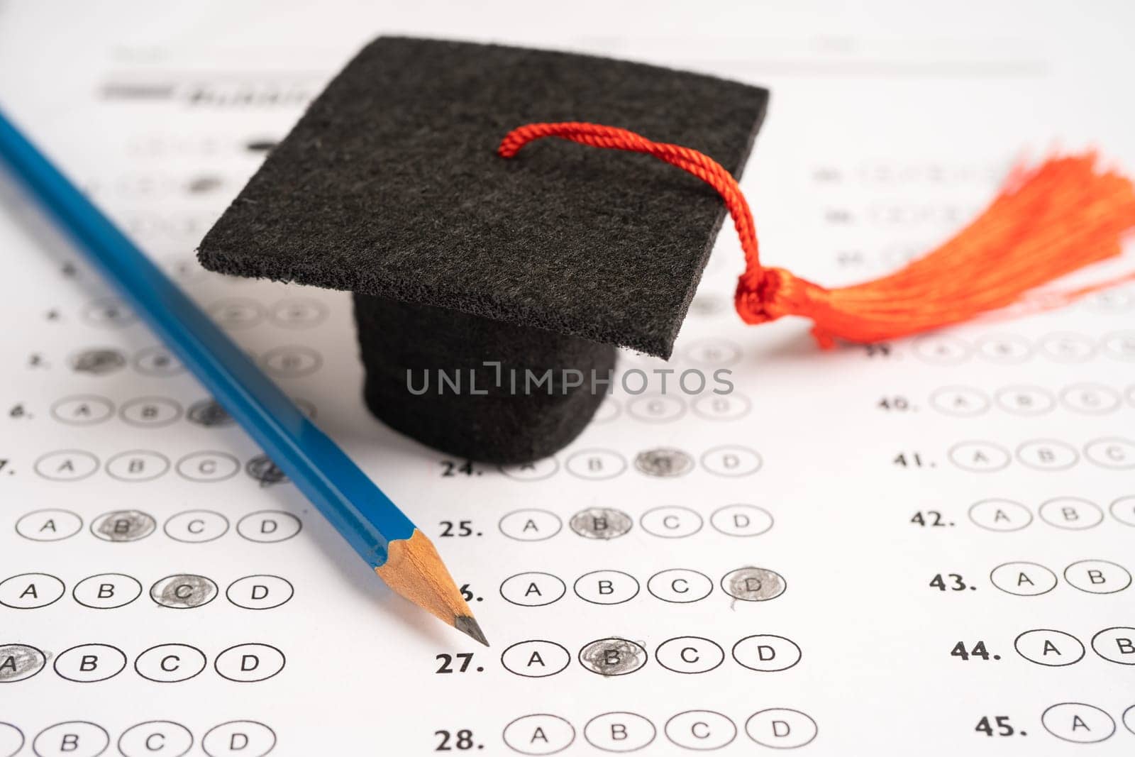 Graduation gap hat and pencil on answer sheet background, Education study testing learning teach concept. by pamai