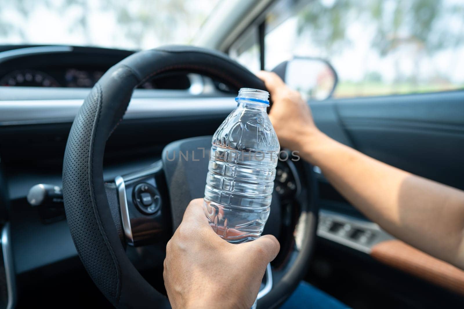 Asian woman driver holding bottle for drink water while driving a car. Plastic hot water bottle cause fire.