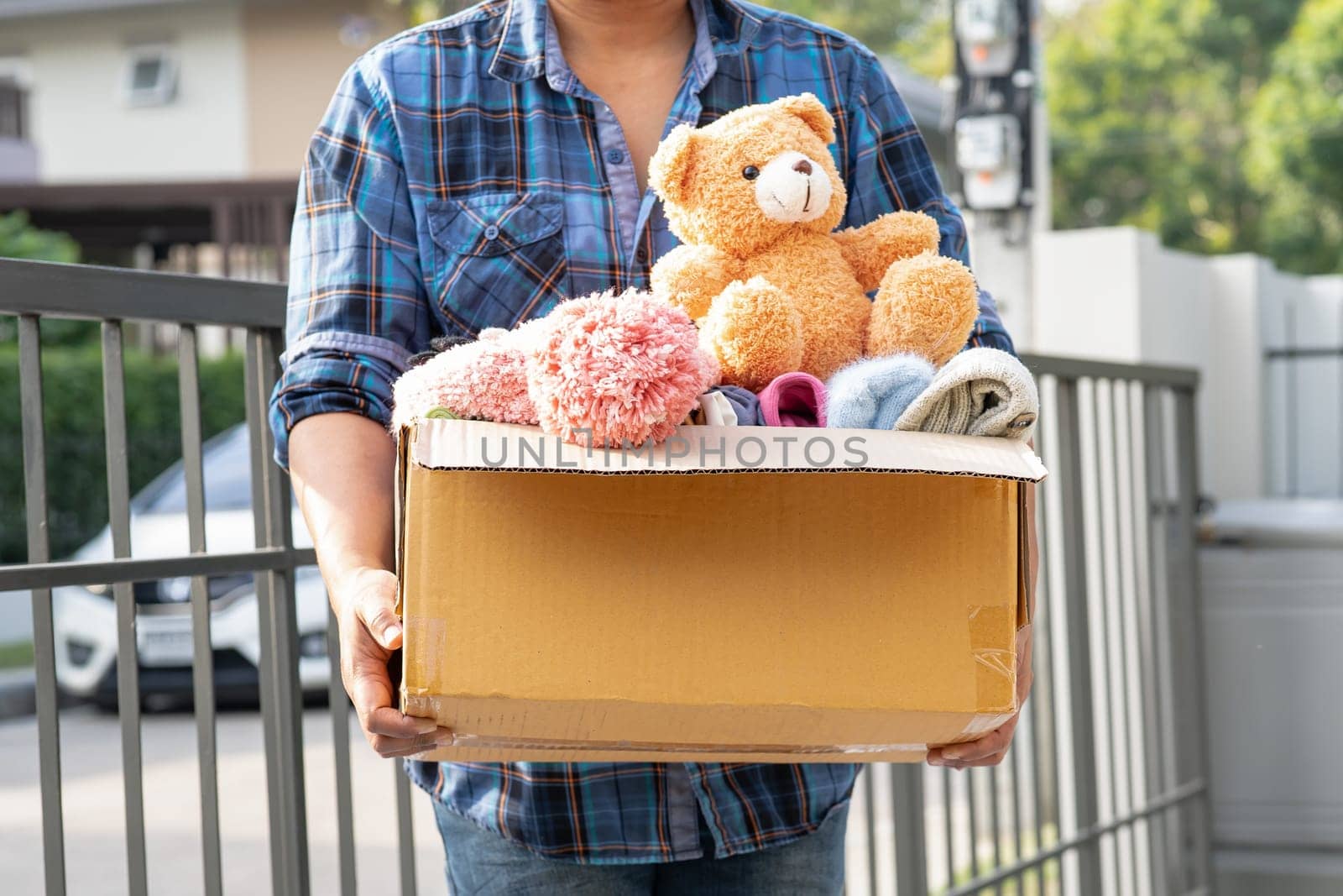 Volunteer woman provide clothing donation box with used clothes and doll to support help for refugee, homeless or poor people in the world.