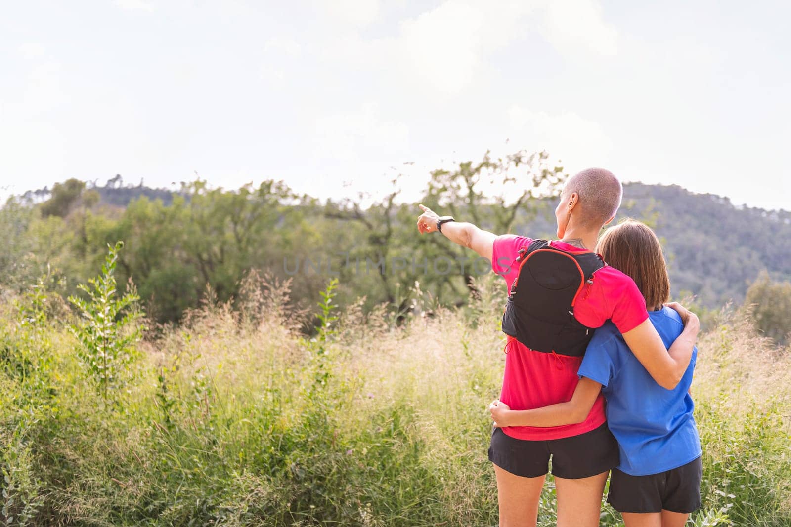 rear view of a mother showing landscape to her daughter after doing sports in the countryside, concept of active lifestyle and sport with kids in the nature, copy space for text