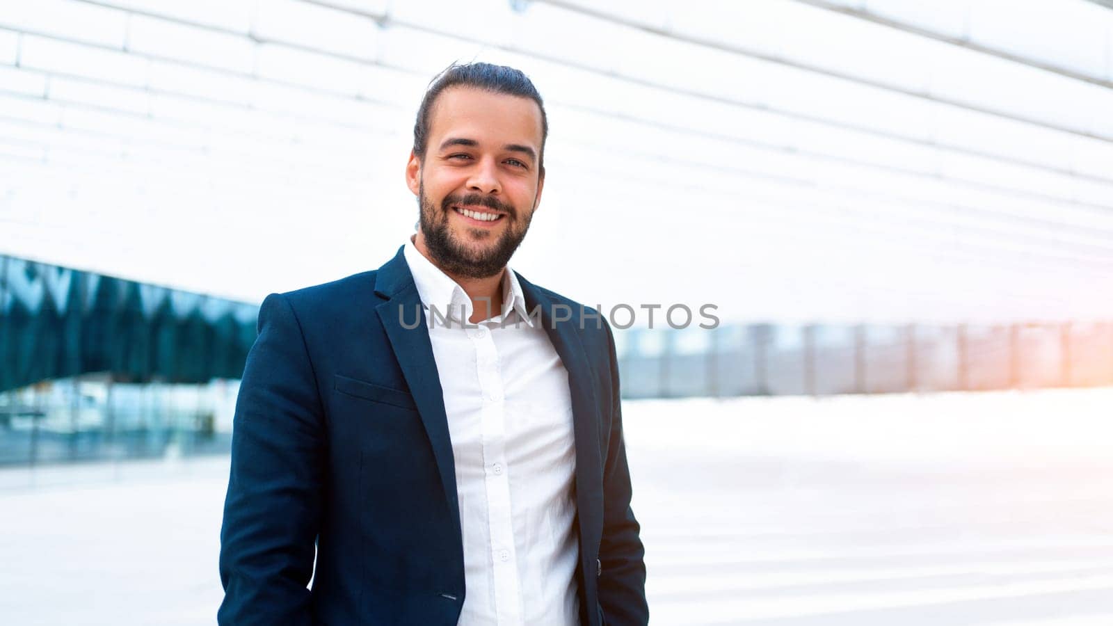 Successful businessman in suit with beard standing in front of office building confidently looking at camera and smile. Hispanic male business person side view portrait. Web banner, Free space