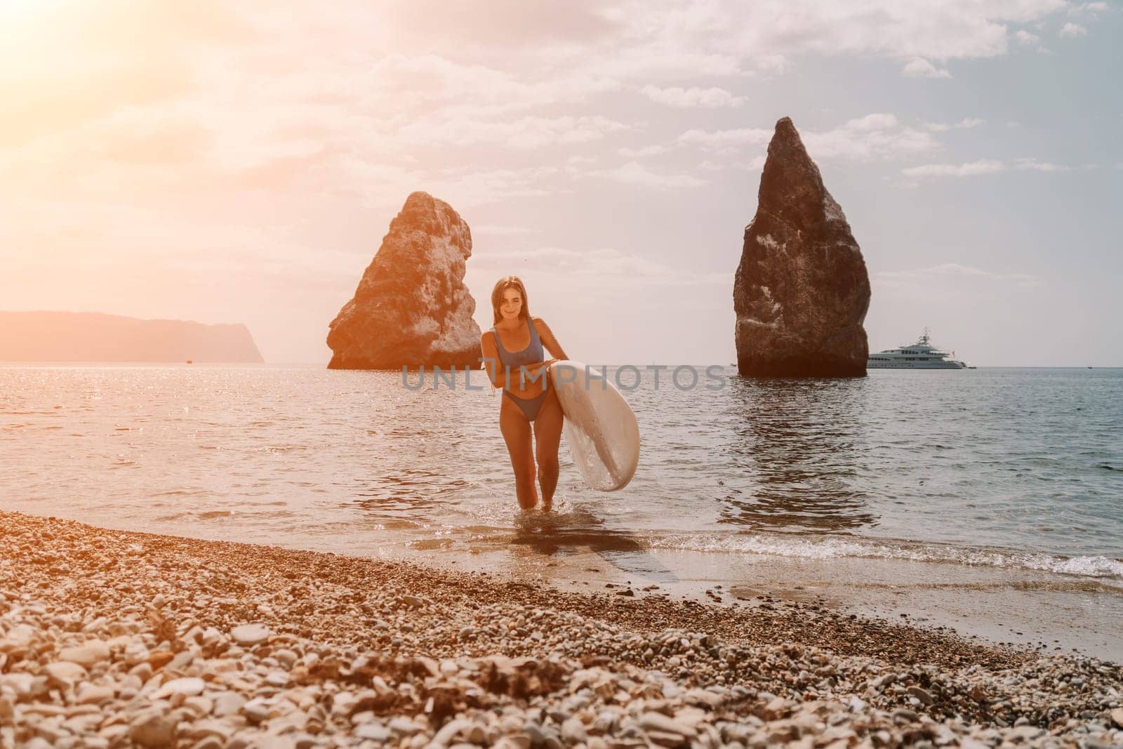 Close up shot of beautiful young caucasian woman with black hair and freckles looking at camera and smiling. Cute woman portrait in a pink bikini posing on a volcanic rock high above the sea