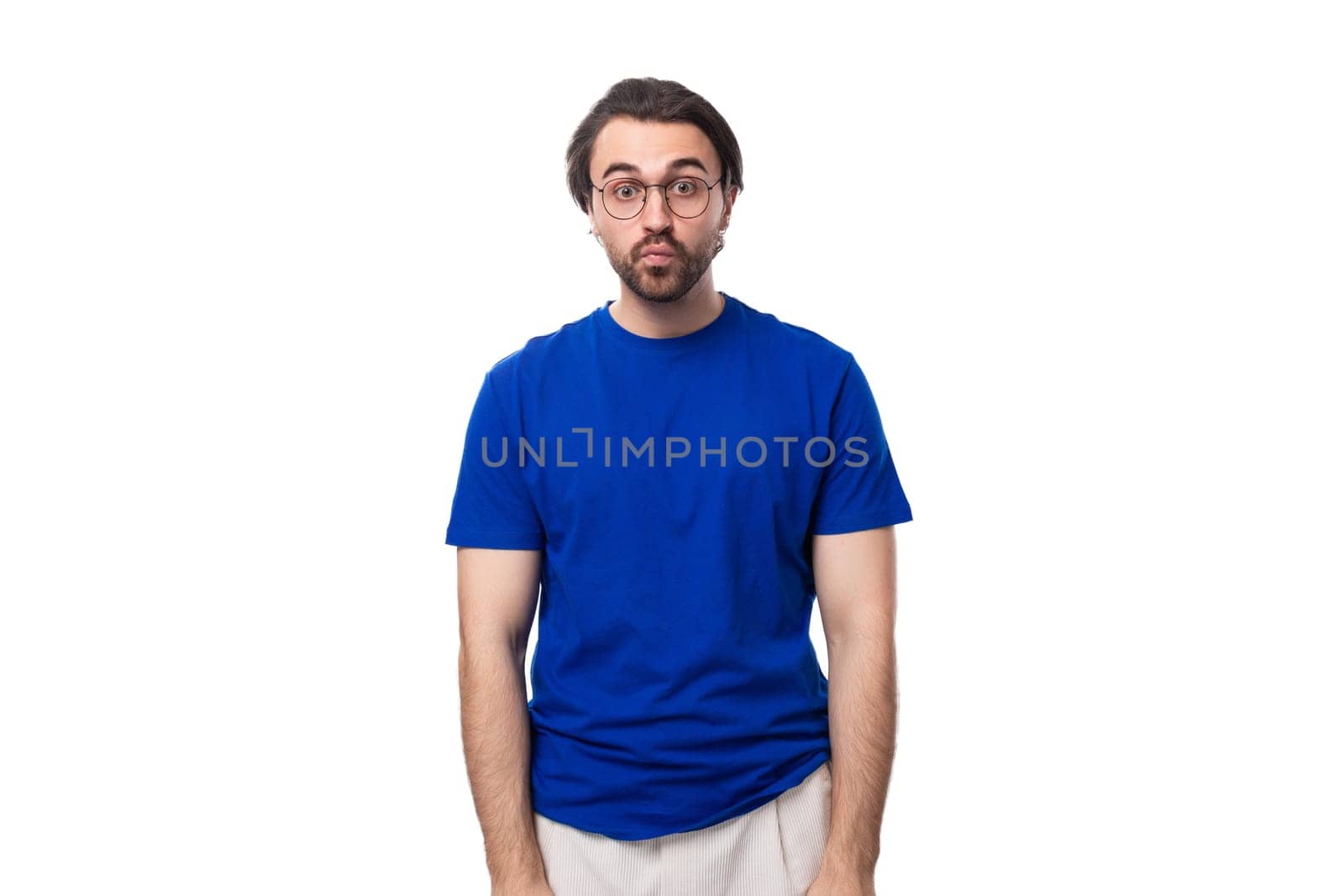 young surprised european brunette man with a beard in glasses dressed in a blue t-shirt.
