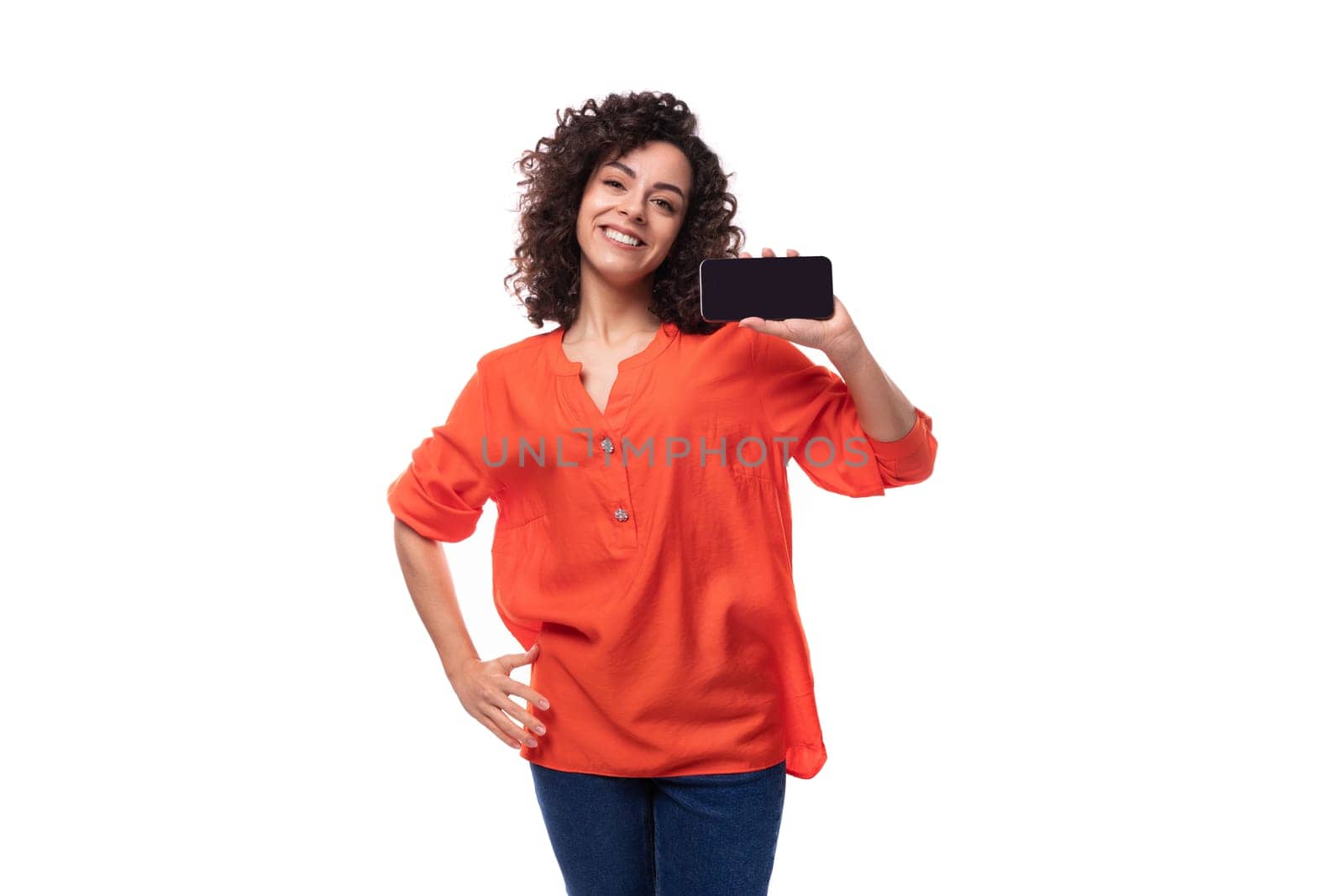 young curly brunette lady dressed in a stylish bright orange shirt shows the smartphone screen by TRMK
