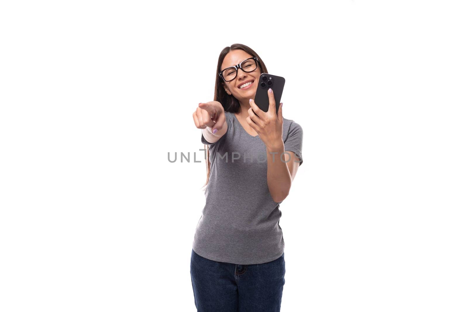 young promoter woman in glasses dressed in a gray t-shirt uses a smartphone on a white background with copy space.