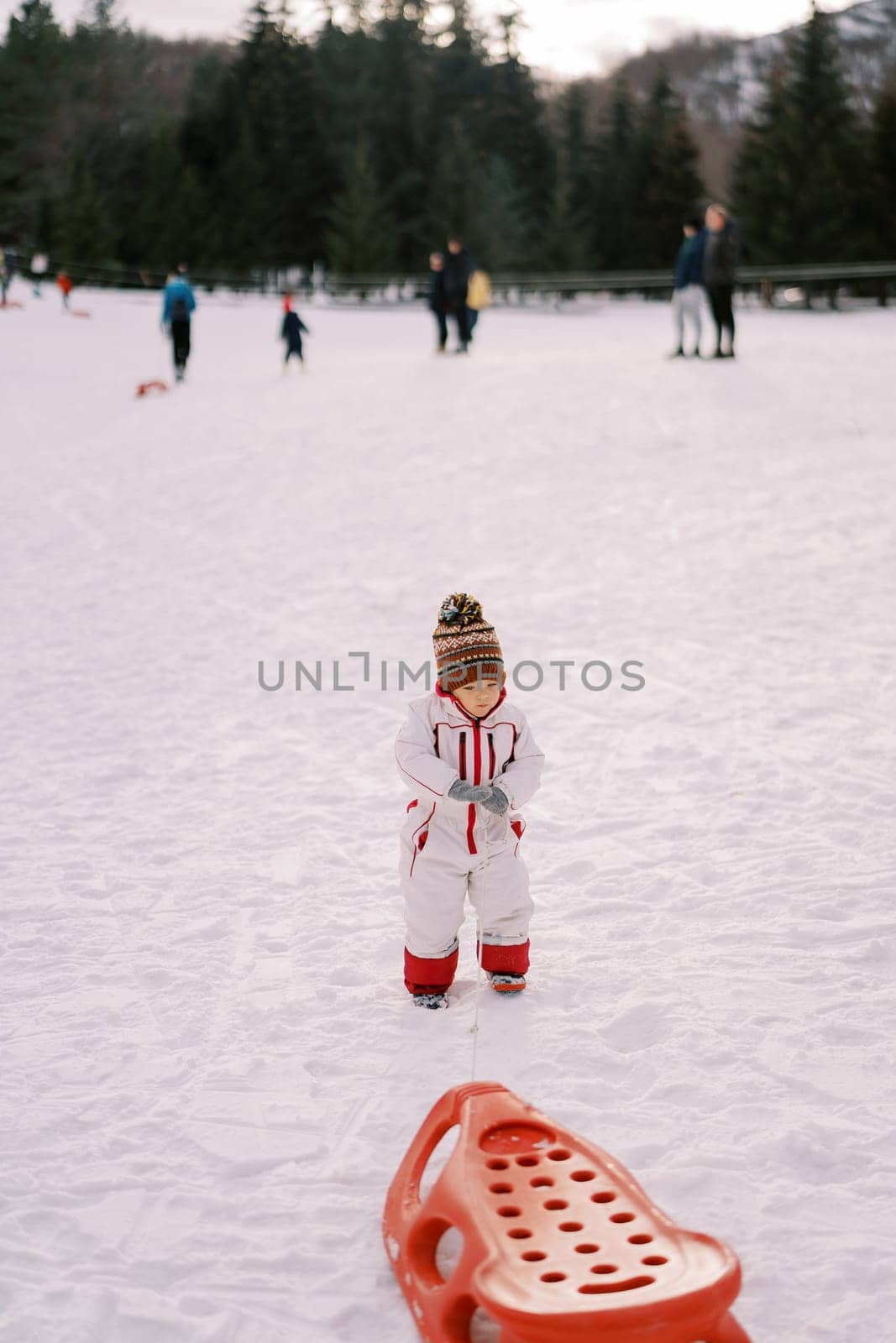 Little girl stands on the snow holding a rope in her hand by Nadtochiy