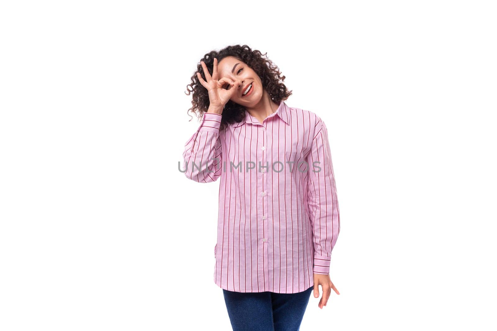 young leader woman with curly hair dressed in a pink shirt and jeans.