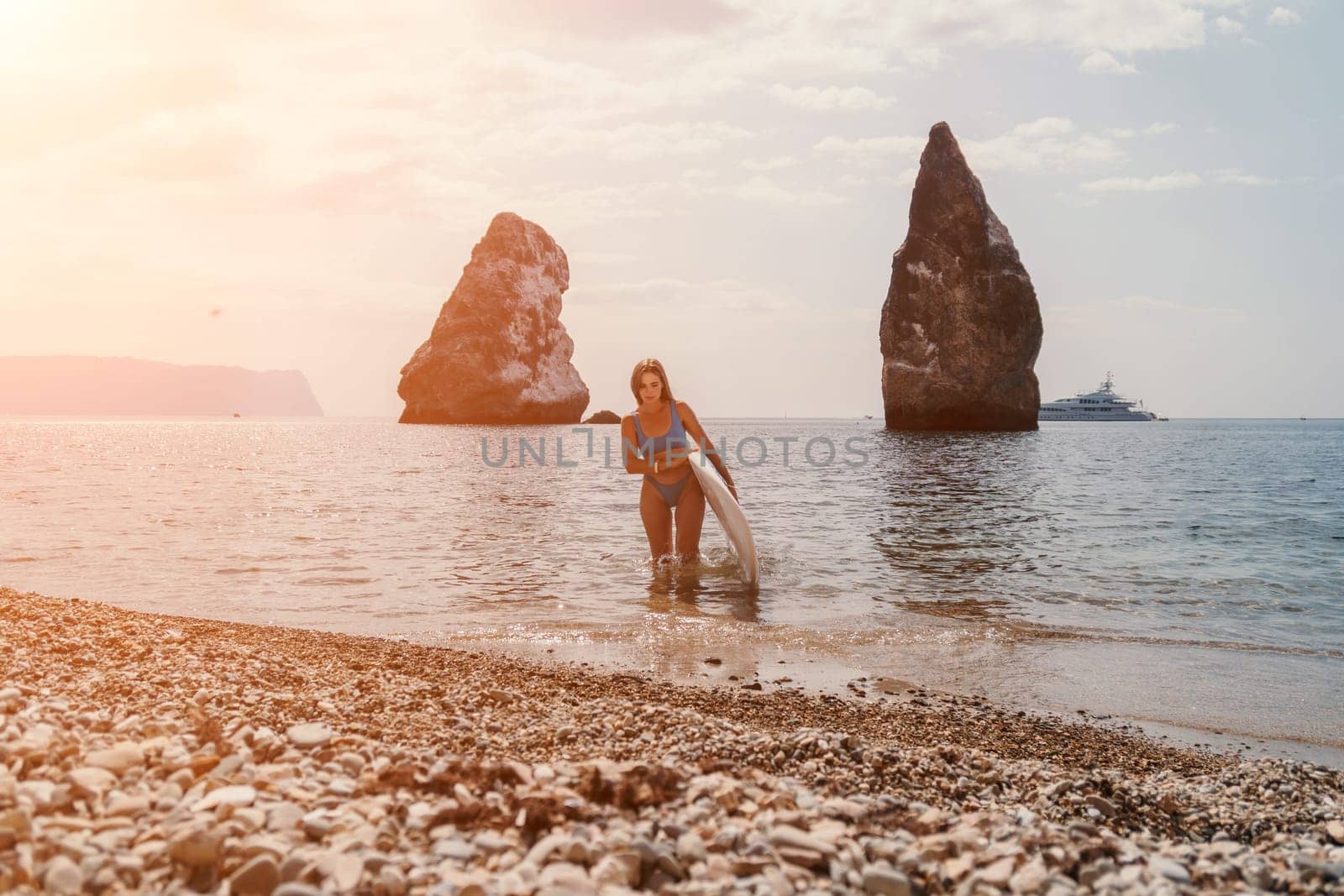 Close up shot of beautiful young caucasian woman with black hair and freckles looking at camera and smiling. Cute woman portrait in a pink bikini posing on a volcanic rock high above the sea