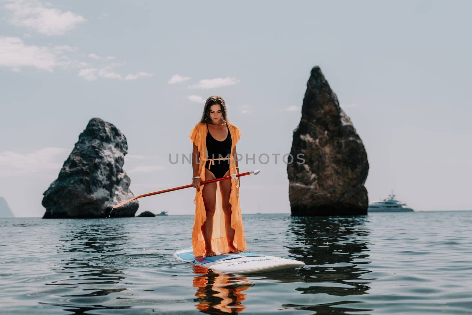 Close up shot of beautiful young caucasian woman with black hair and freckles looking at camera and smiling. Cute woman portrait in a pink bikini posing on a volcanic rock high above the sea