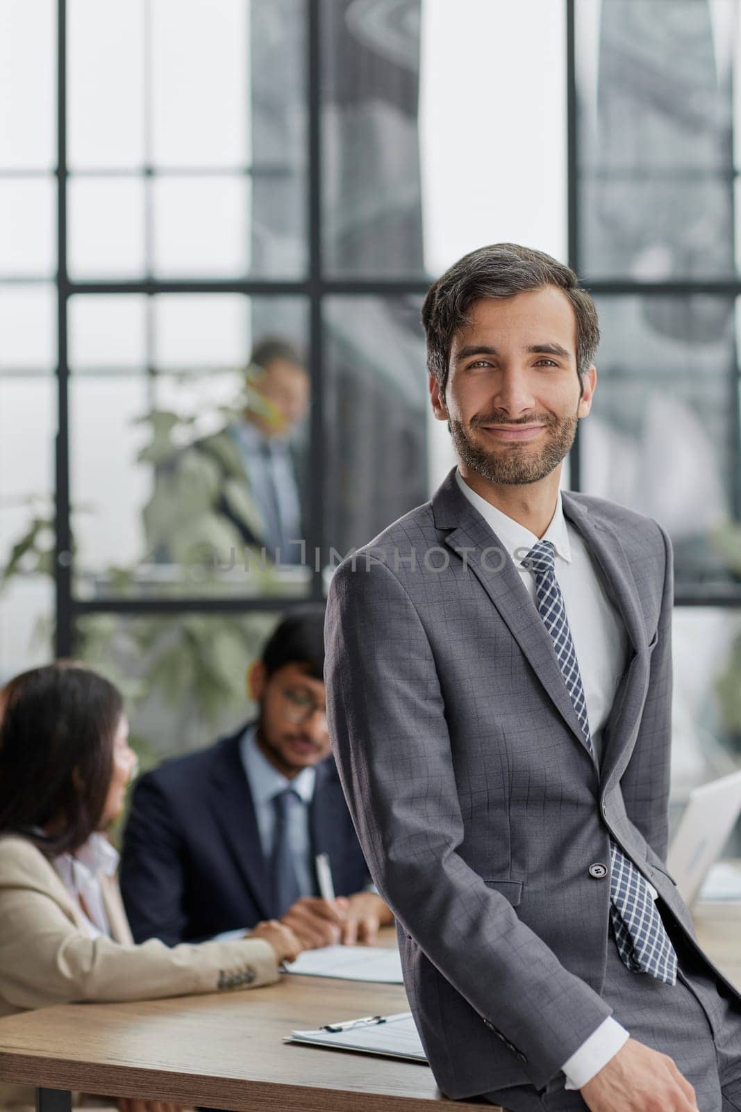 professional businessman, executive director of the company, sitting at the table in the office, with colleagues in the background