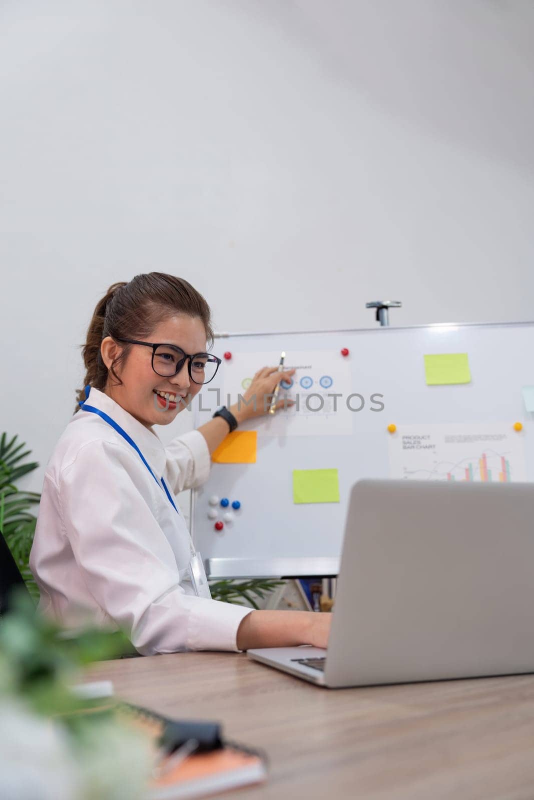 Business young woman asian explain business data on white board in office . The businesswoman report on laptop information progress of a business project to partner to determine market strategy.