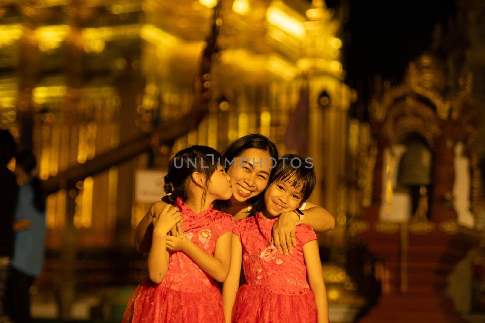 Happy family, mother and her children pose for the camera at Golden pagoda at Wat Phra That Haripunchai Woramahawihan in Lamphun, north of Thailand. by TEERASAK