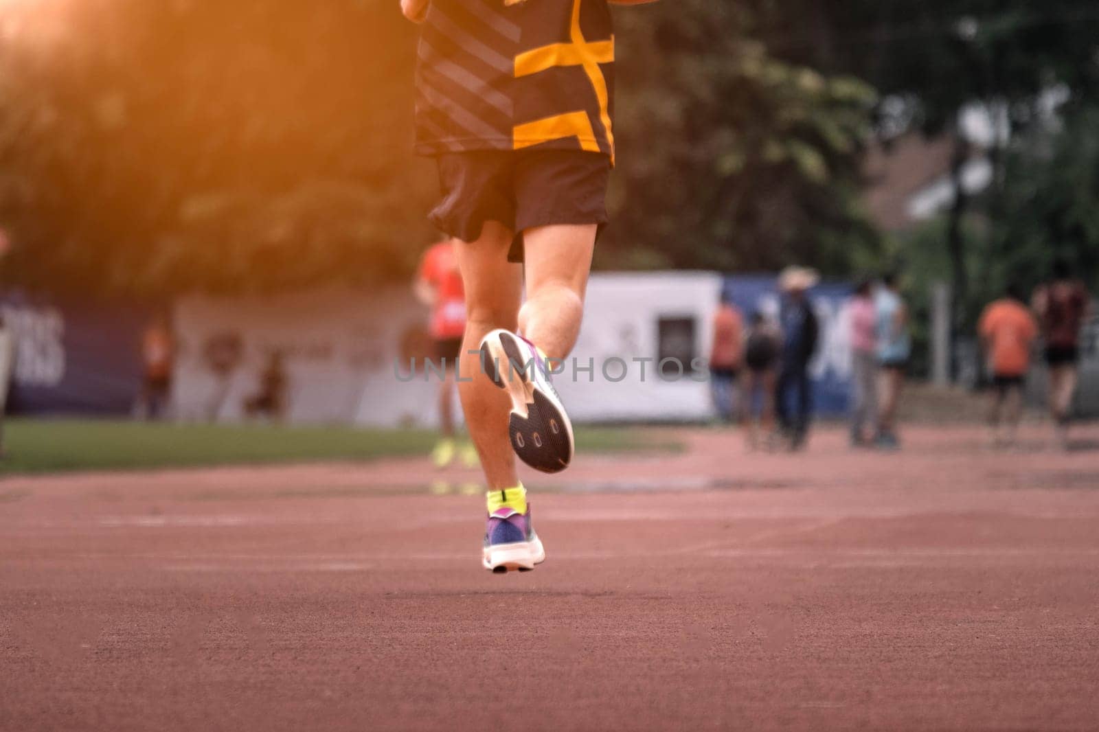 The feet of an athlete running outdoors at the racetrack. Fit young man is running on the race track. Male runner in sportswear running on stadium track with red coating outdoors.