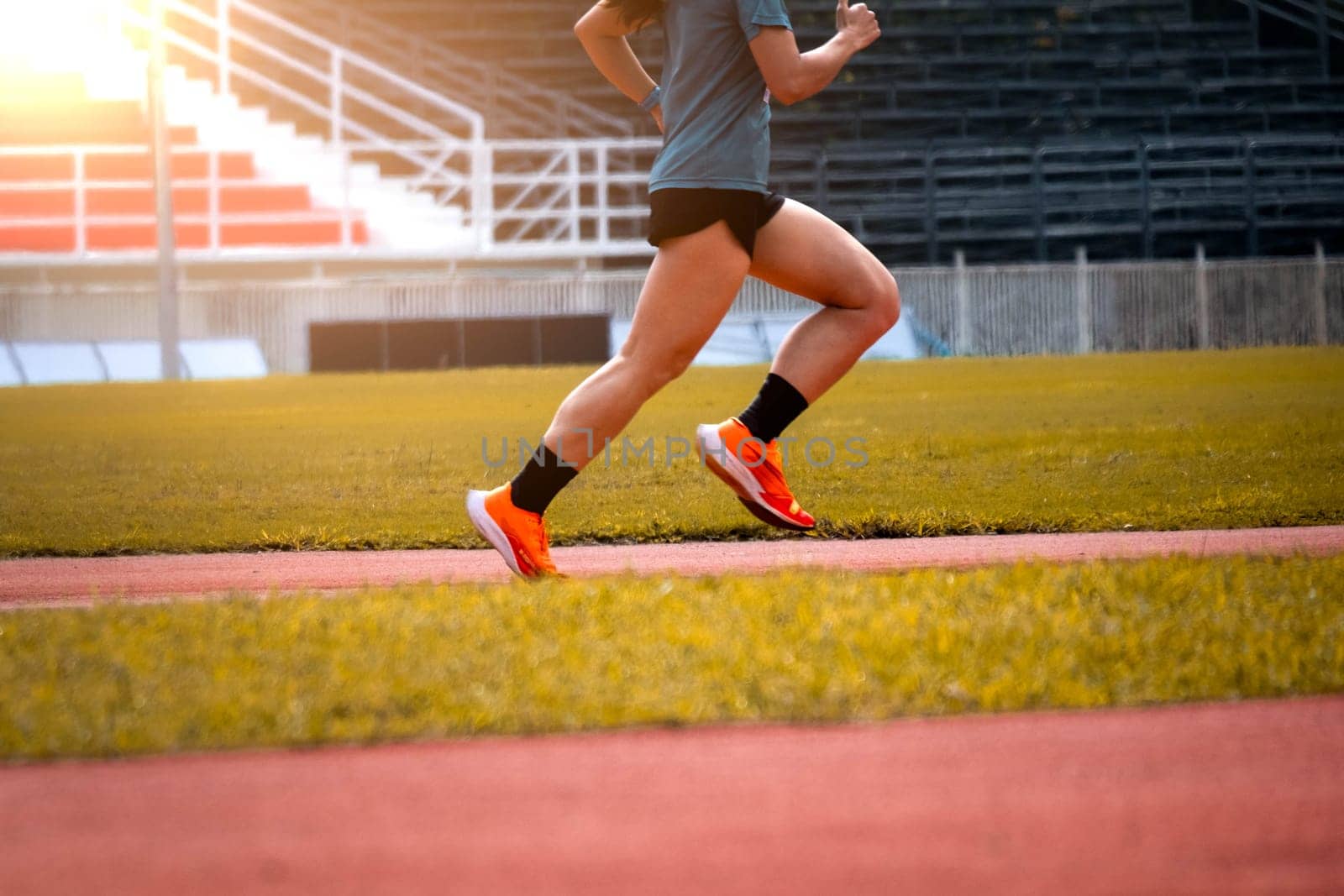 The feet of an athlete running outdoors at the racetrack. Fit young man is running on the race track. Male runner in sportswear running on stadium track with red coating outdoors. by TEERASAK