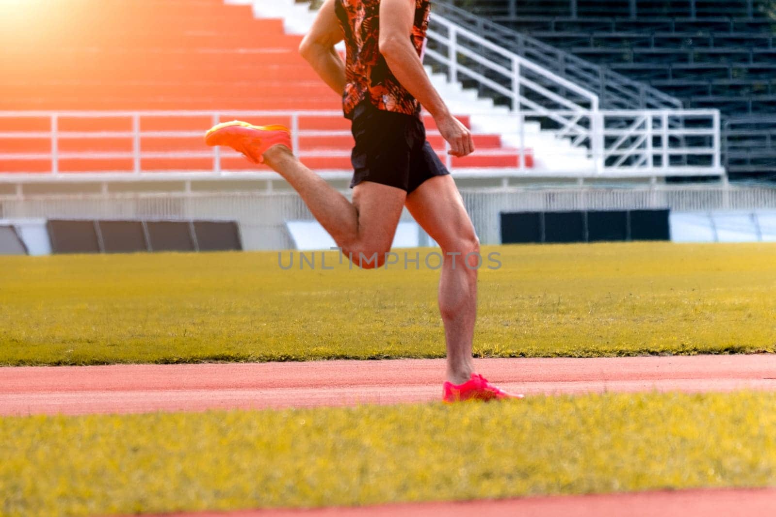 The feet of an athlete running outdoors at the racetrack. Fit young man is running on the race track. Male runner in sportswear running on stadium track with red coating outdoors.