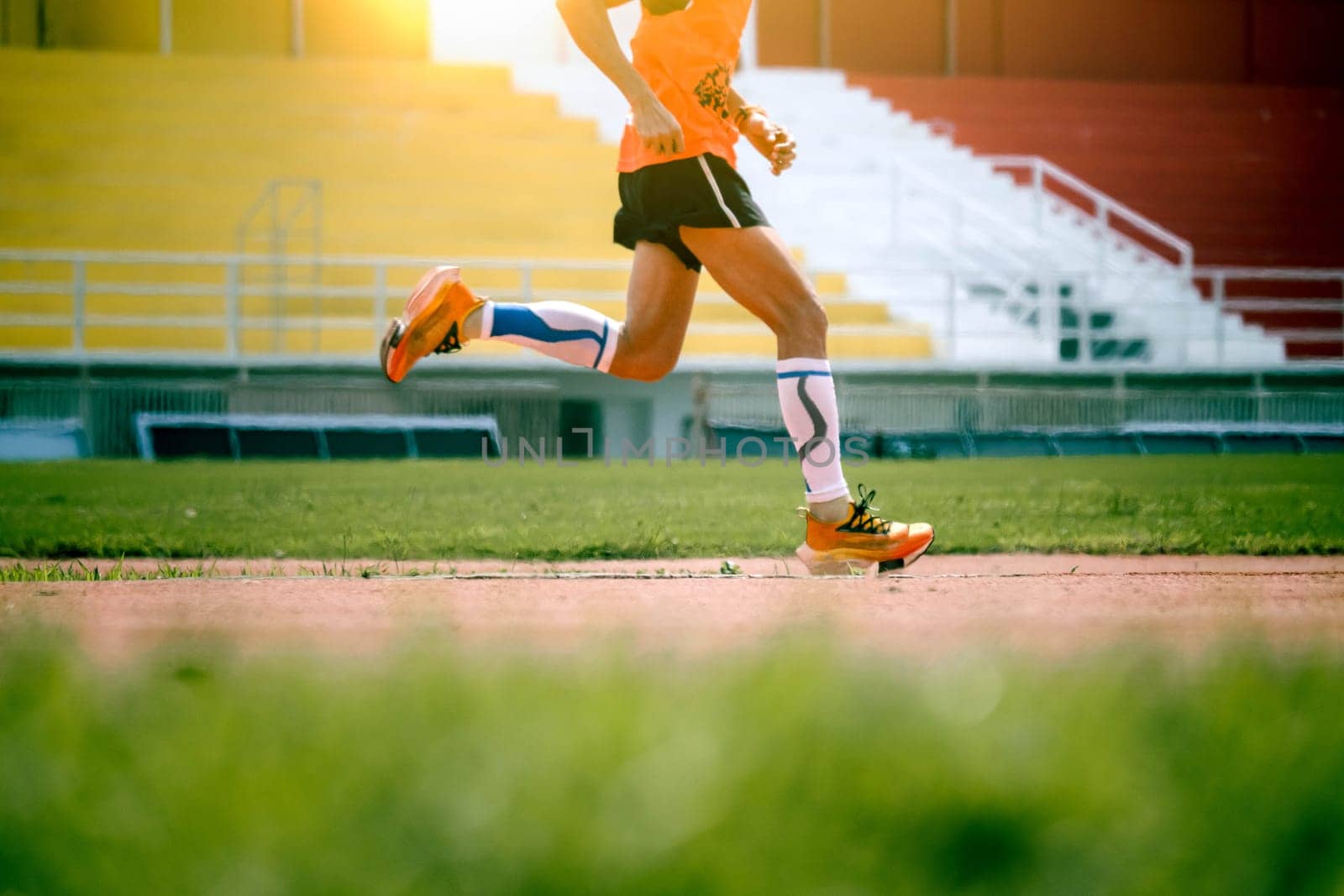 The feet of an athlete running outdoors at the racetrack. Fit young man is running on the race track. Male runner in sportswear running on stadium track with red coating outdoors.