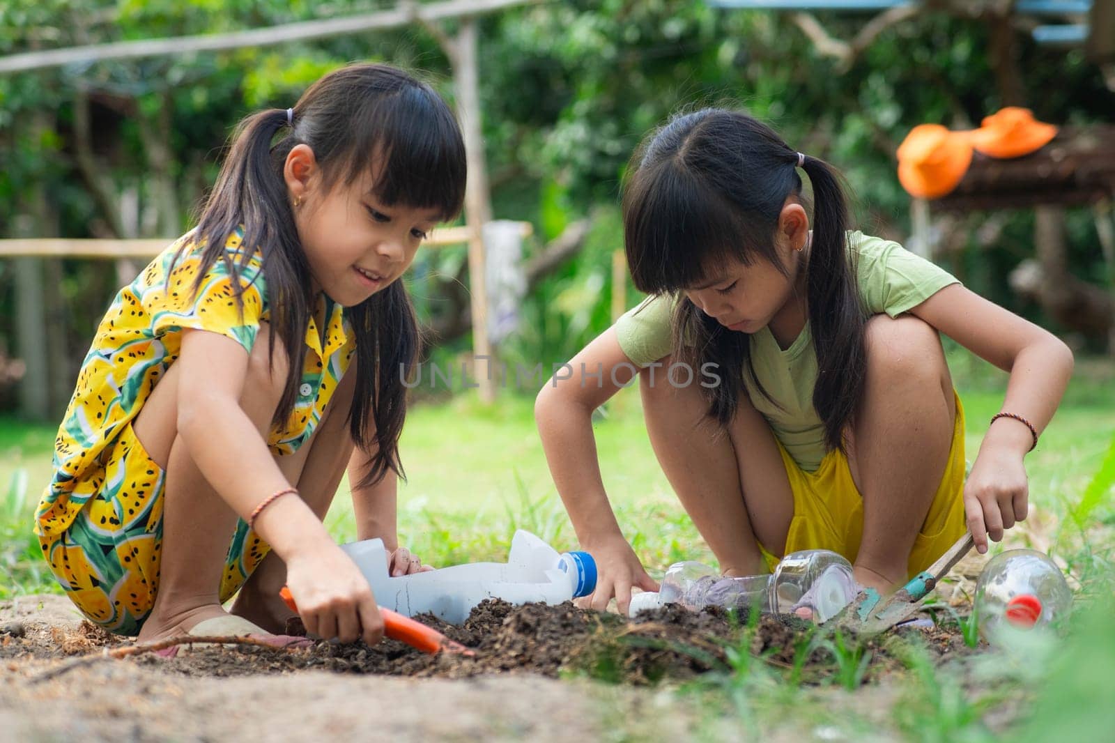 Little girl planting plants in pots from recycled water bottles in the backyard. Recycle water bottle pot, gardening activities for children. Recycling of plastic waste by TEERASAK