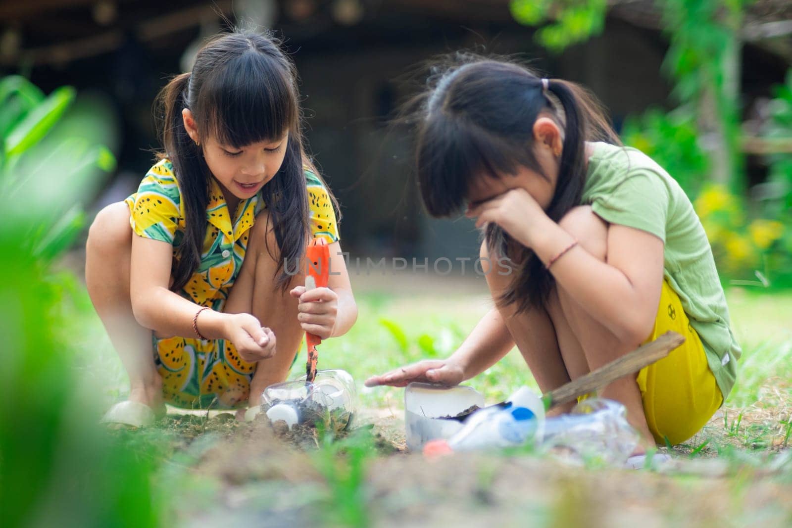 Little girl planting plants in pots from recycled water bottles in the backyard. Recycle water bottle pot, gardening activities for children. Recycling of plastic waste by TEERASAK