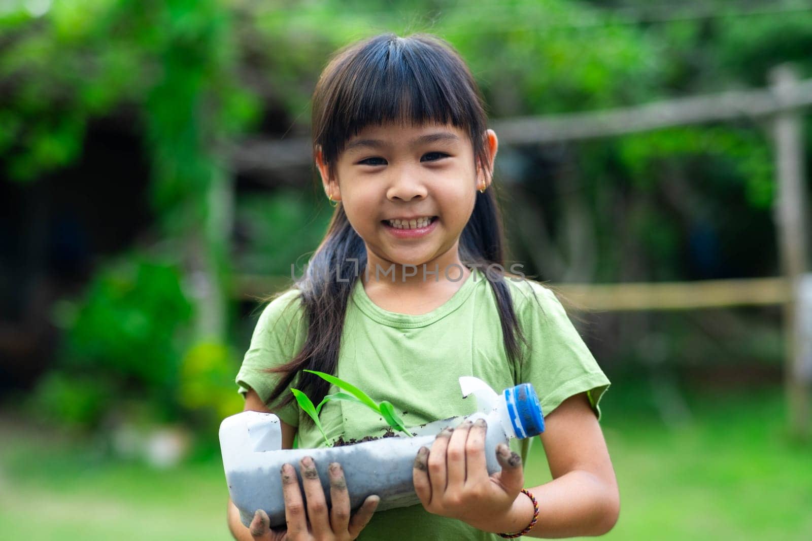 Little girl shows saplings grown in recycled plastic bottles. Recycle water bottle pot, gardening activities for children. Recycling of plastic waste by TEERASAK