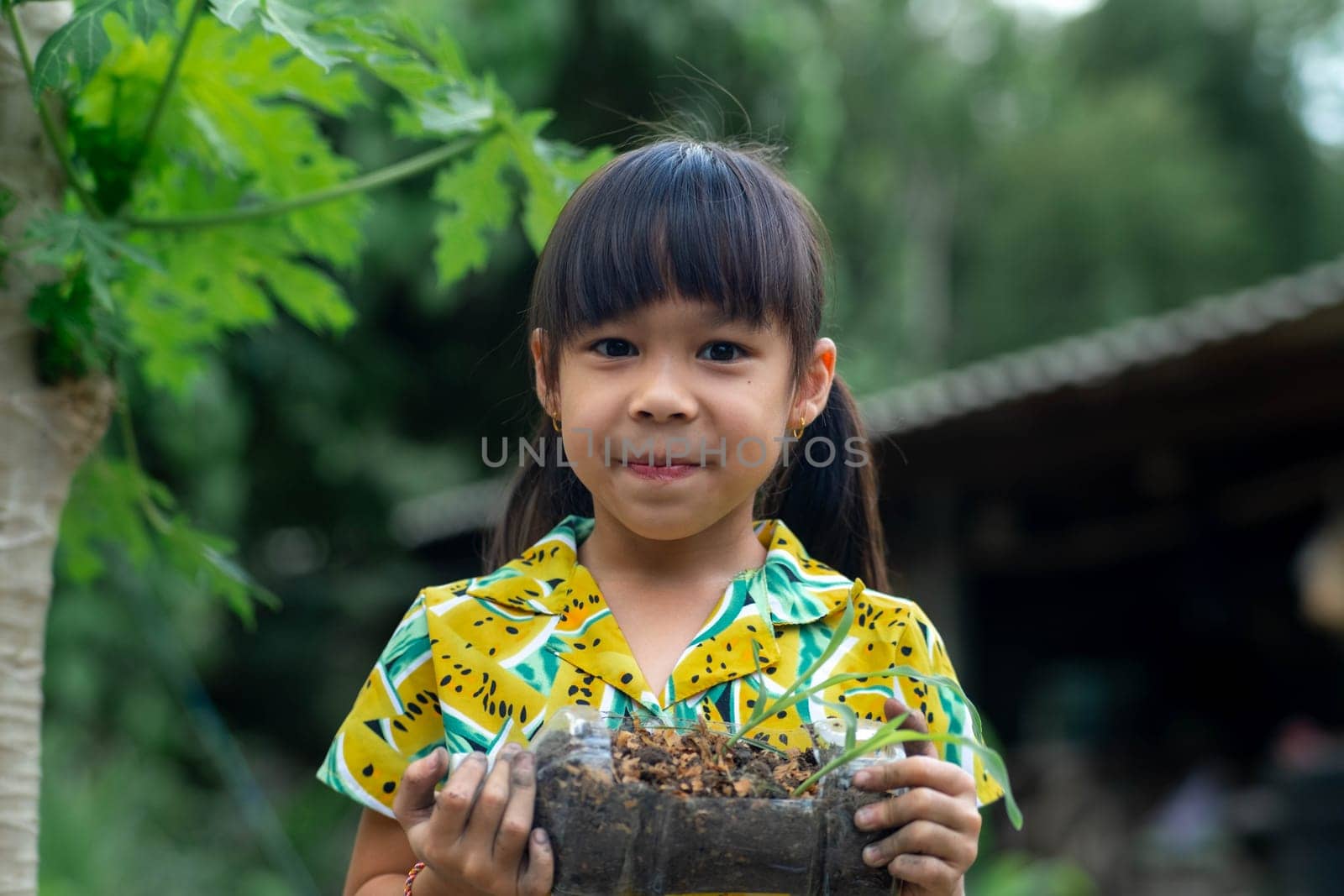 Little girl shows saplings grown in recycled plastic bottles. Recycle water bottle pot, gardening activities for children. Recycling of plastic waste by TEERASAK